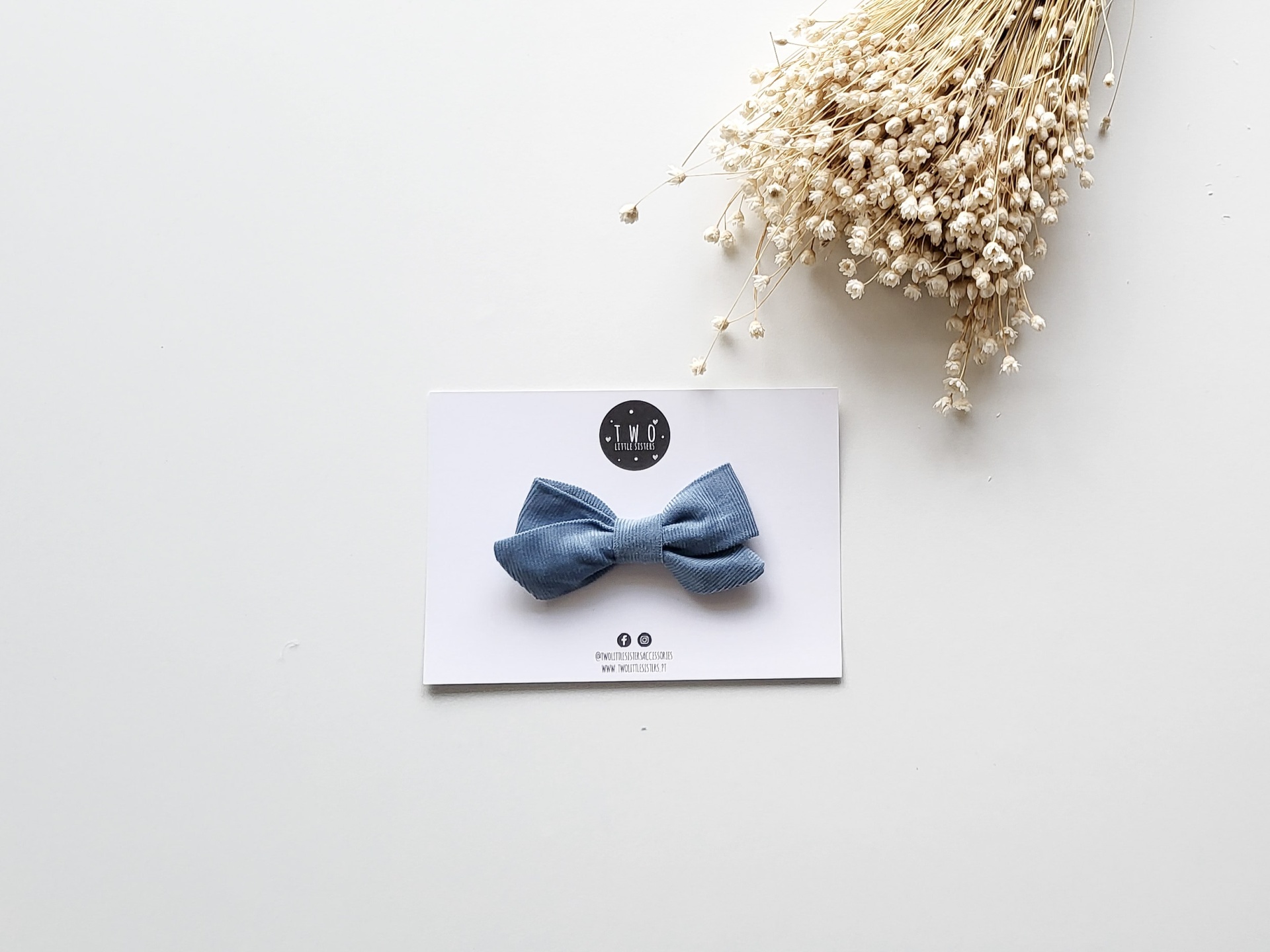 Laço azul de tecido numa cartolina branca com logótipo 'MINI' e flores secas no fundo branco