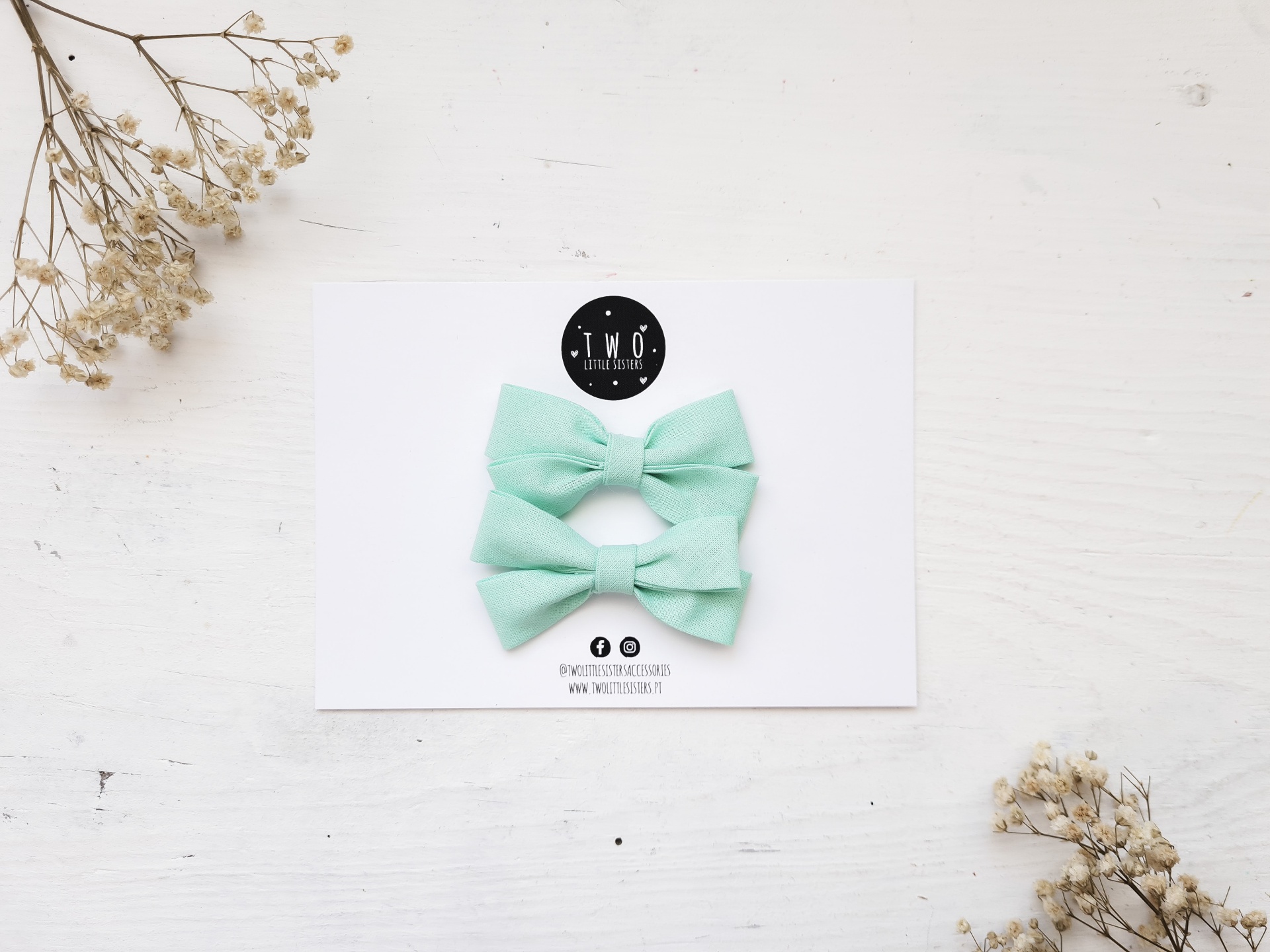 Dois laços de tecido verde claro em cartão branco com logo T.M.O.