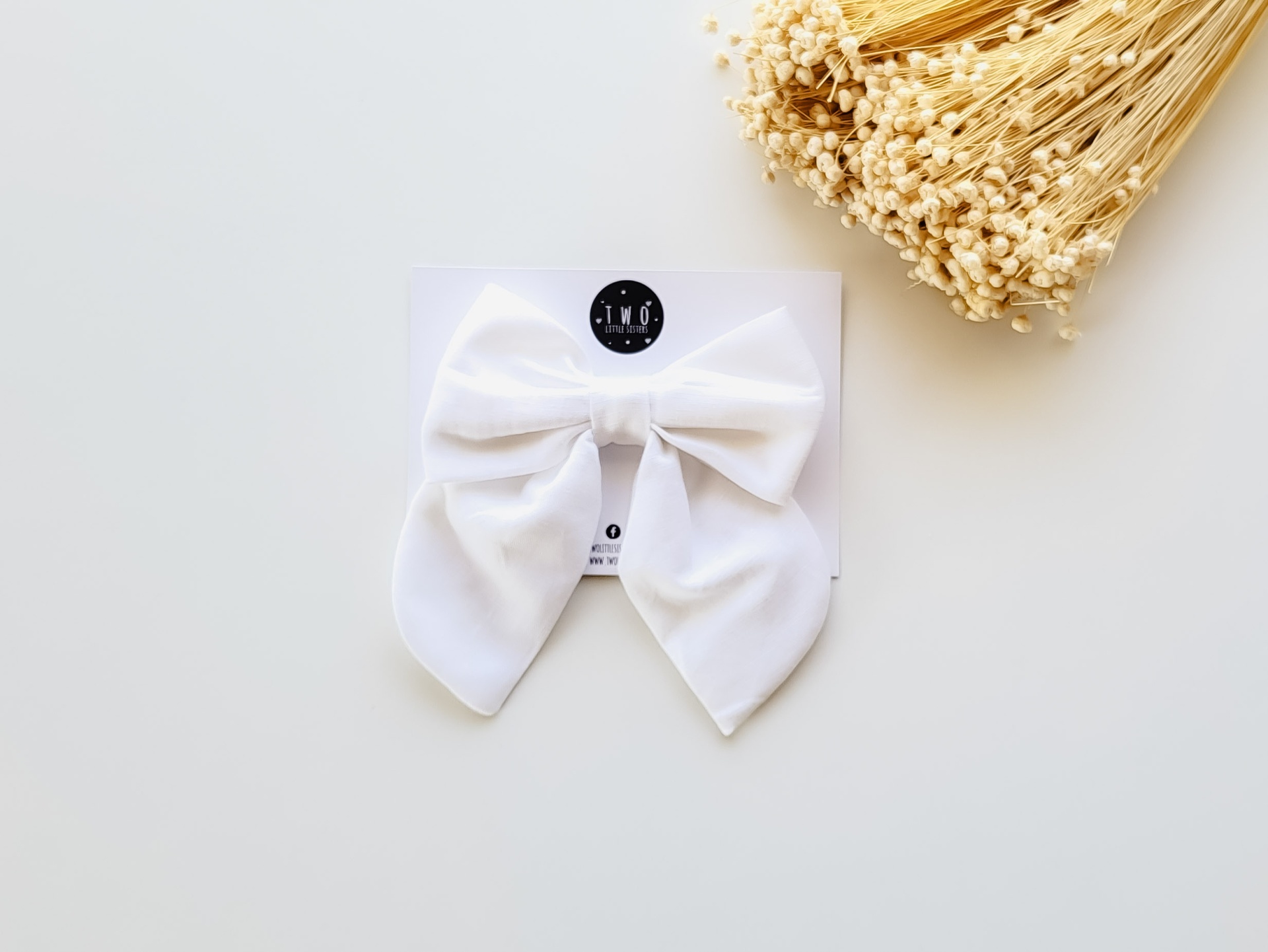 Gravata branca de tecido sobre cartão branco com etiqueta preta e flores secas ao lado