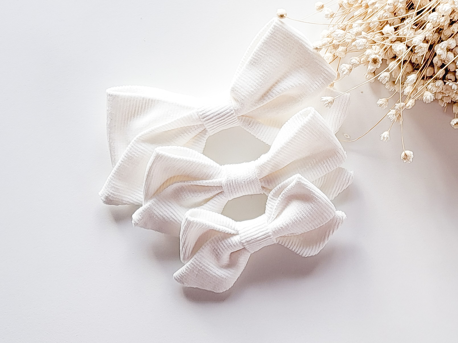 Três laços brancos de tecido com flores secas ao lado