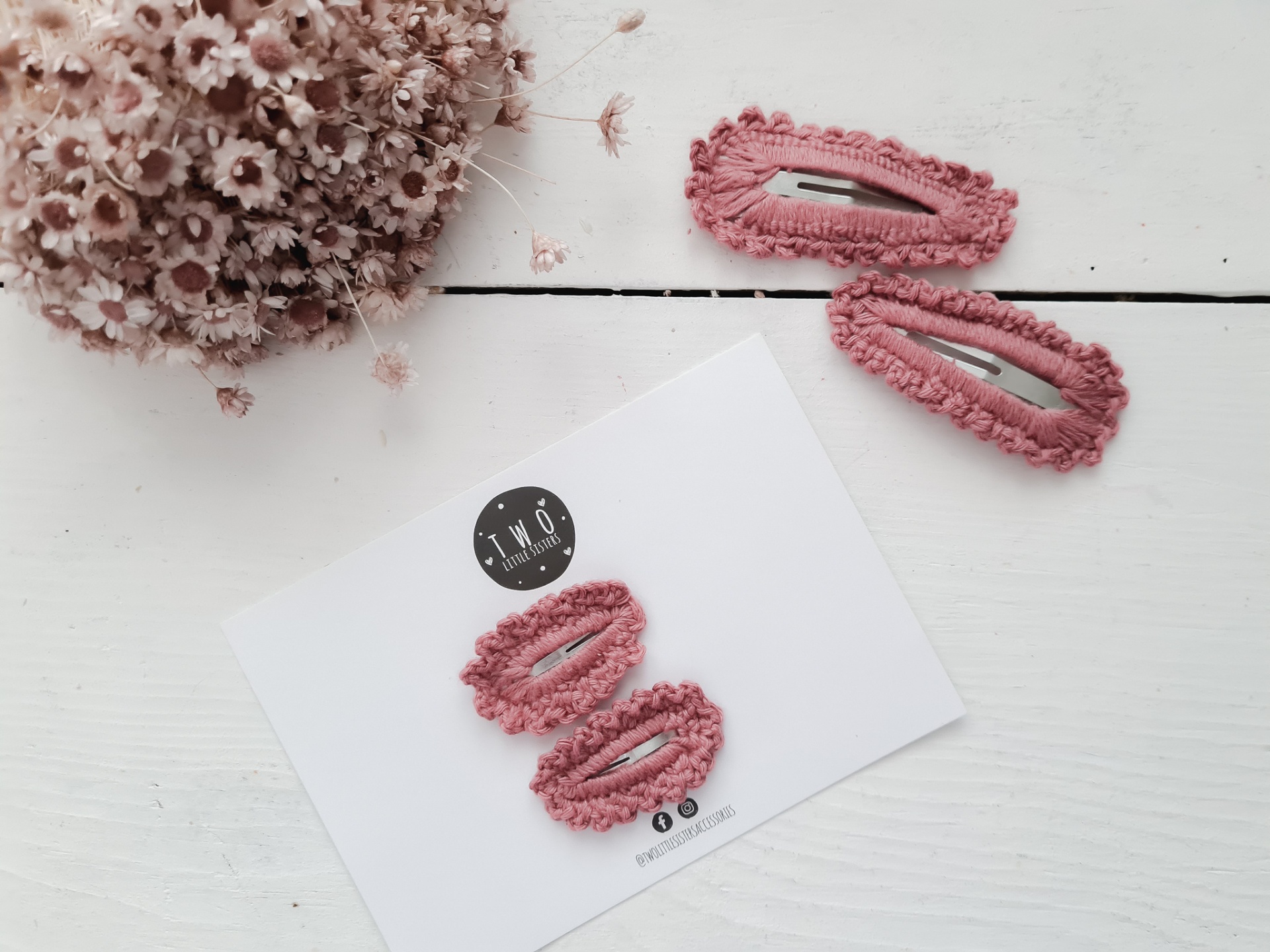 Dois pares de molas de cabelo rosa felpuda com cartão da marca TWO numa mesa branca com flores secas.