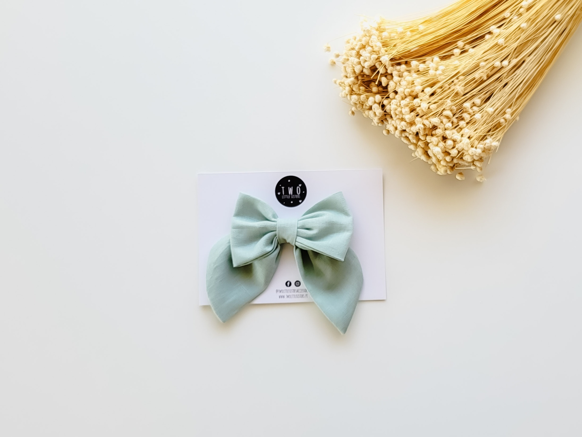 Laço de cabelo verde-menta com cartão e flores secas no fundo branco