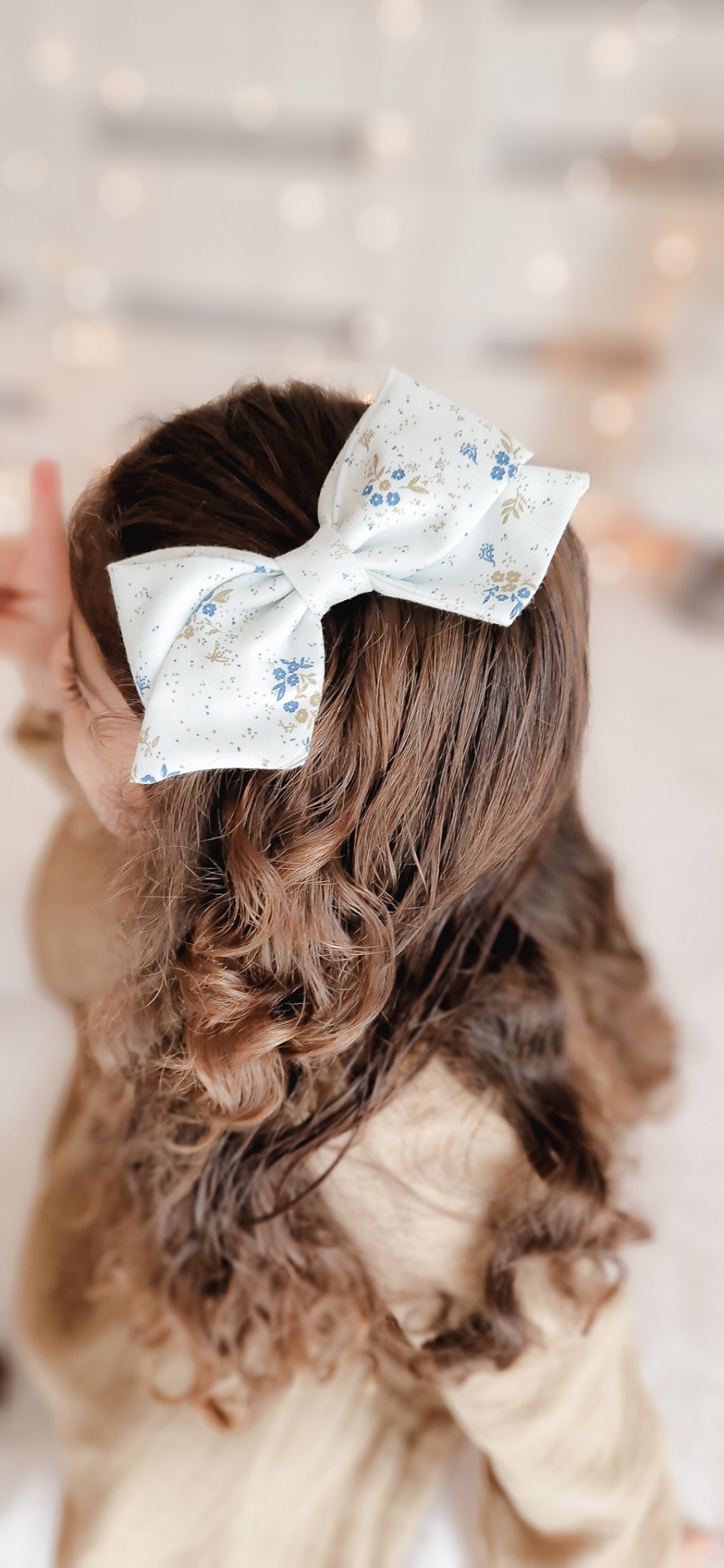Laço branco com flores azuis no cabelo cacheado de uma criança