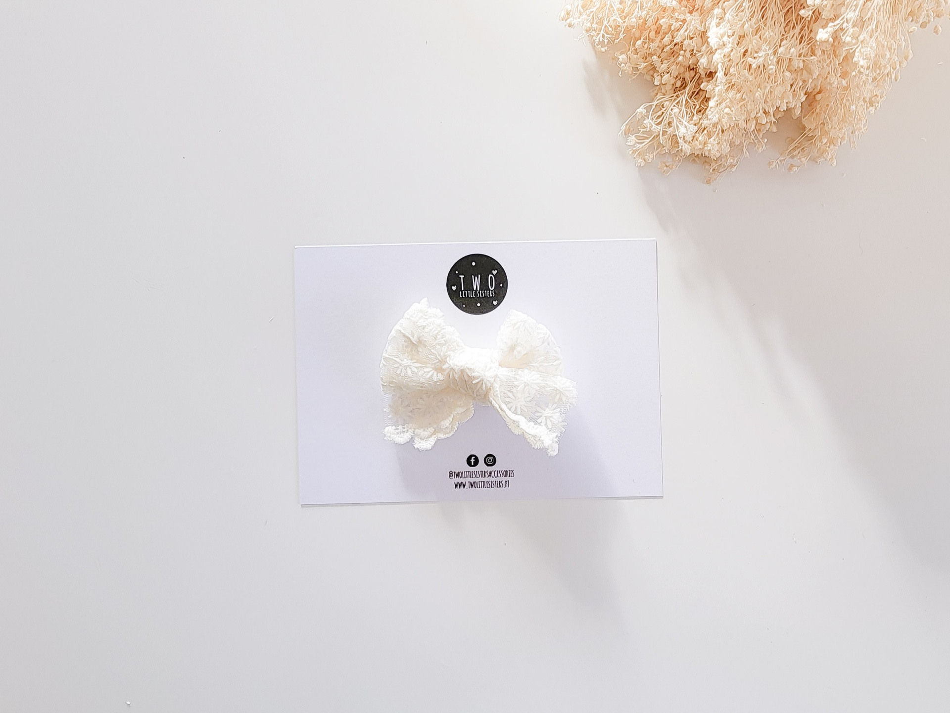 Laço de cabelo branco em renda sobre cartão branco com logotipo TNR