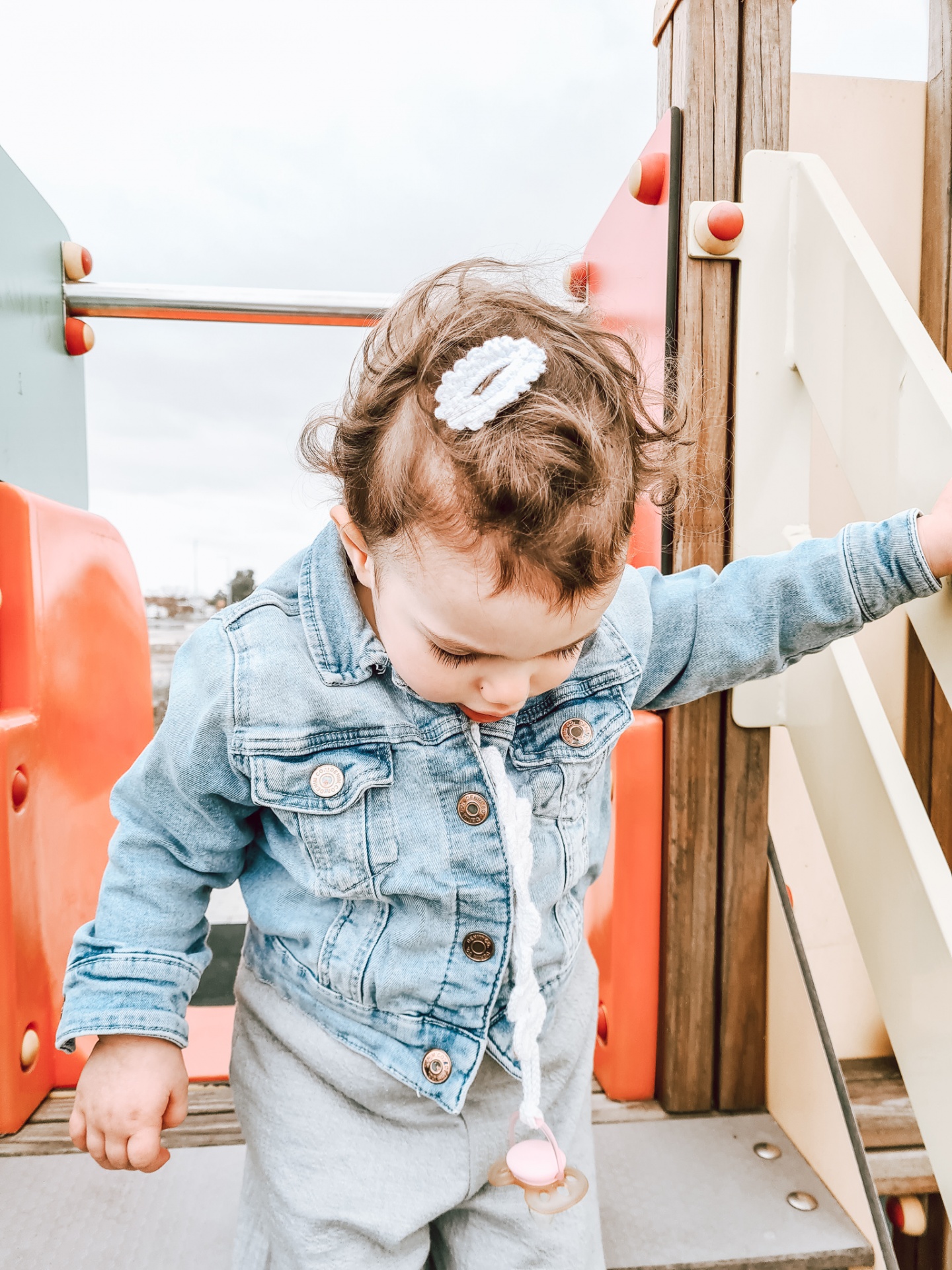 Criança com casaco de ganga e chupeta em parque infantil