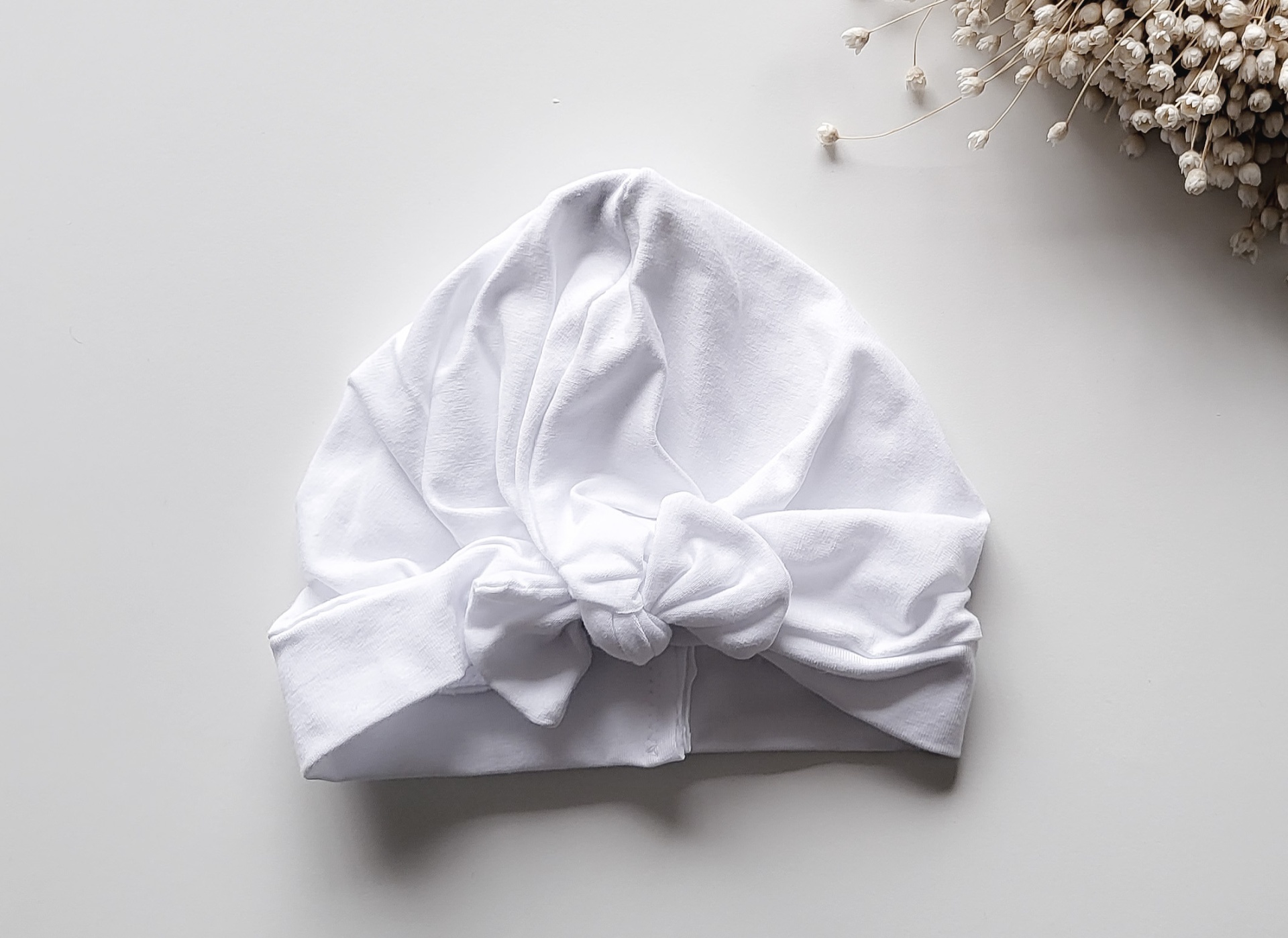Touca branca de tecido macio com nó frontal sobre superfície branca