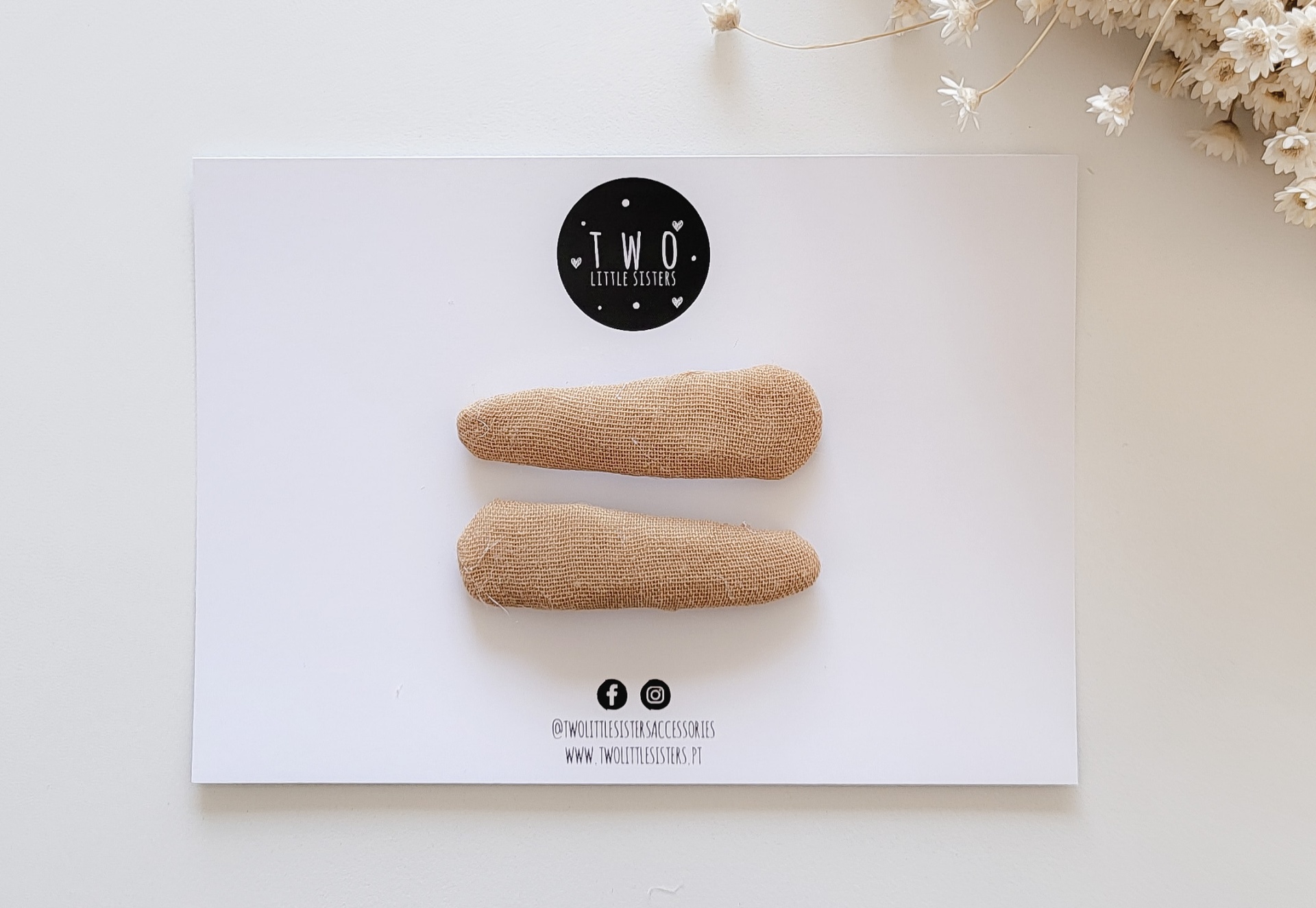 Duas presilhas de cabelo castanhas sobre um cartão branco com texto e selo preto