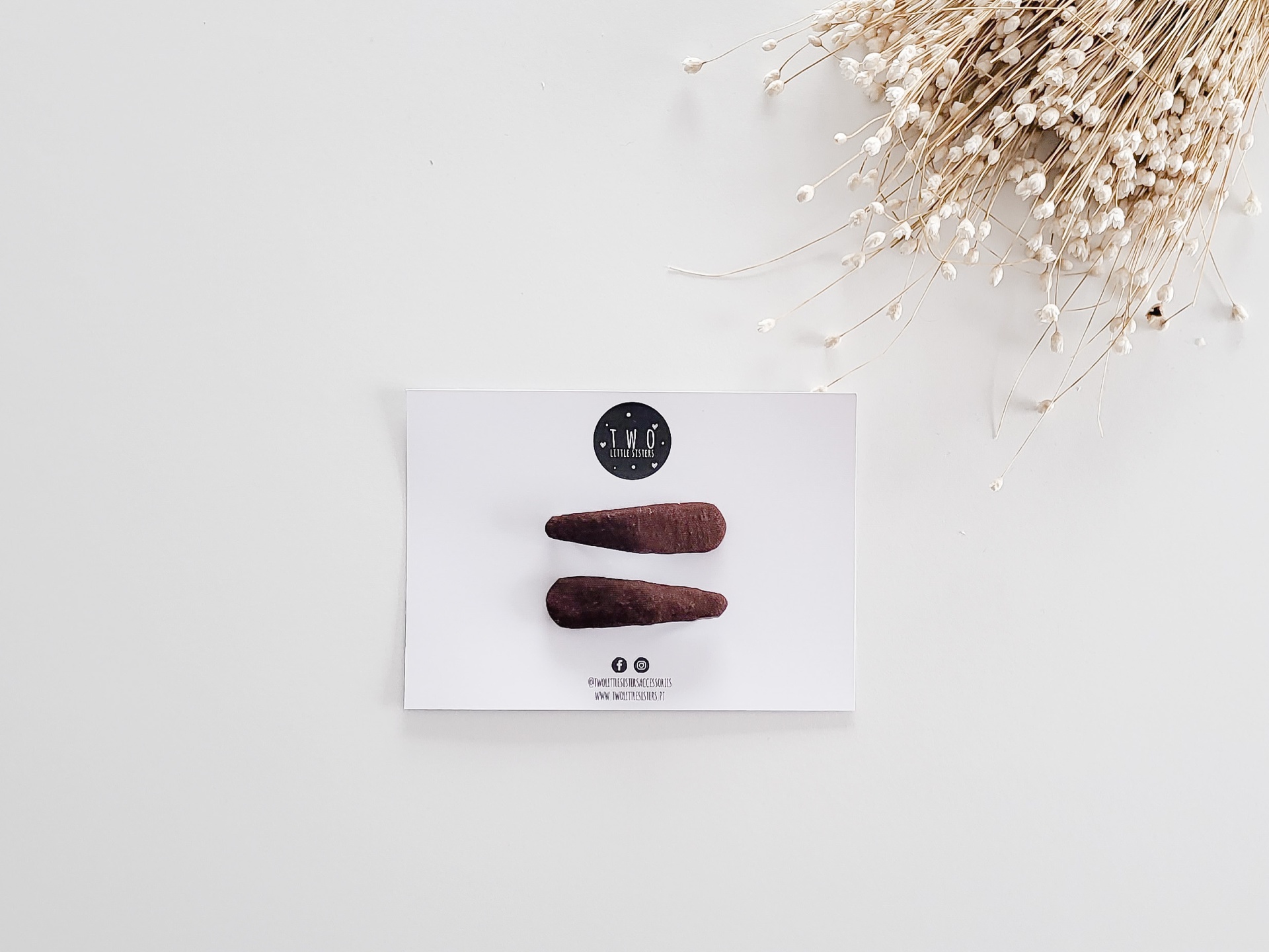 Dois ganchos de cabelo de feltro castanho escuro em cartão branco com logótipo e texto, fundo branco e ramo seco
