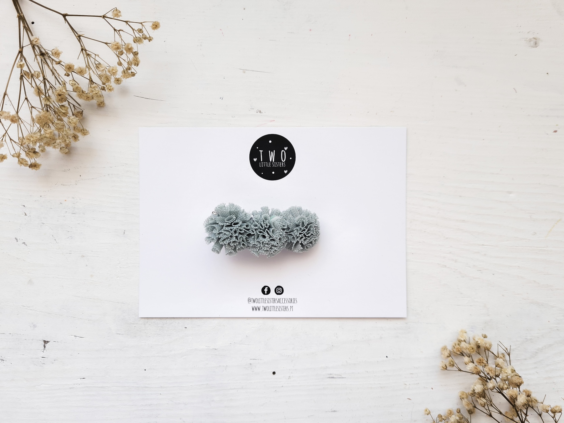 Mola de cabelo cinzenta com pompons sobre papel branco com logo TMO Fashion Accessory