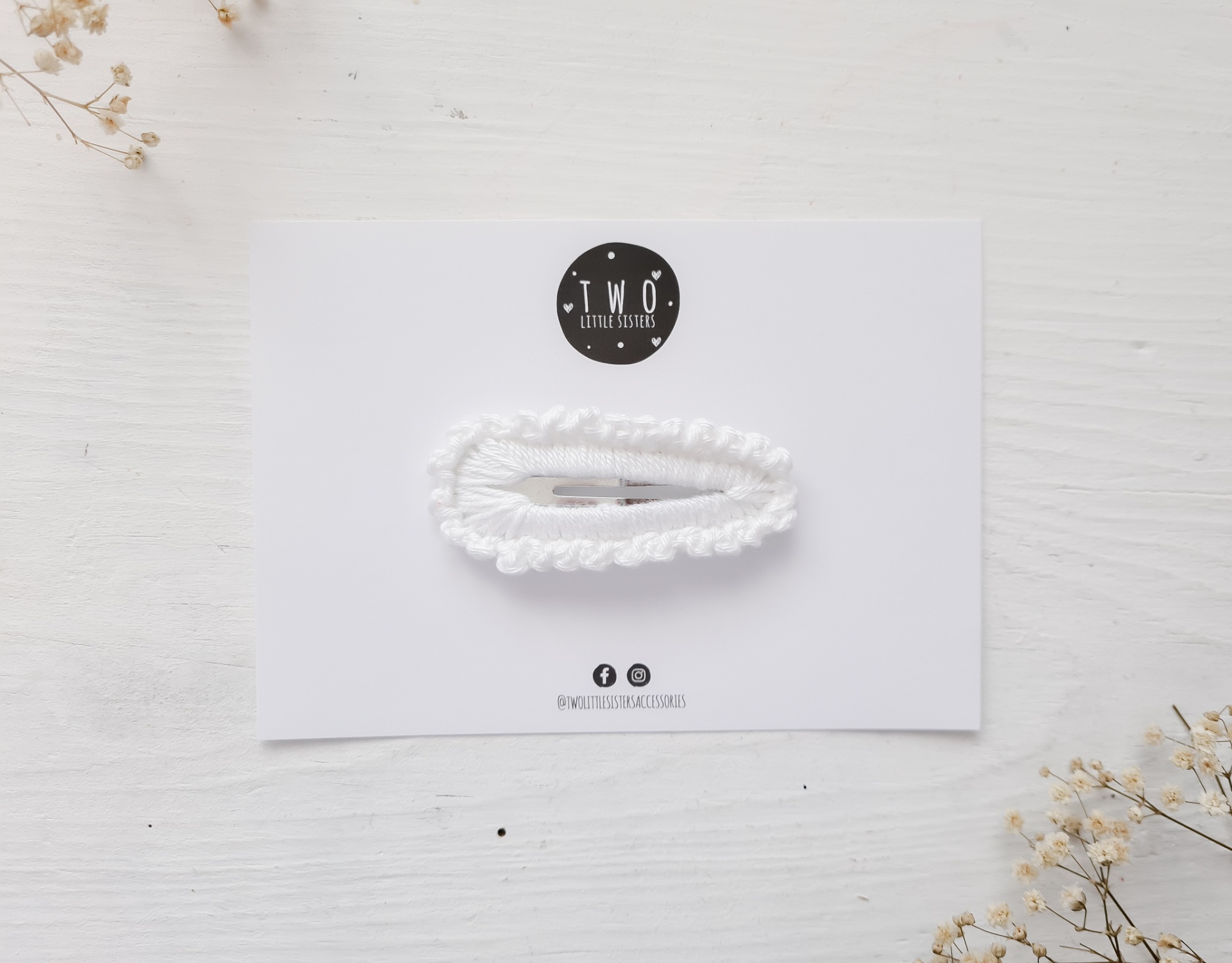 Elástico de cabelo branco franzido em cartão branco com logo Two Little Rooms e flores secas no fundo