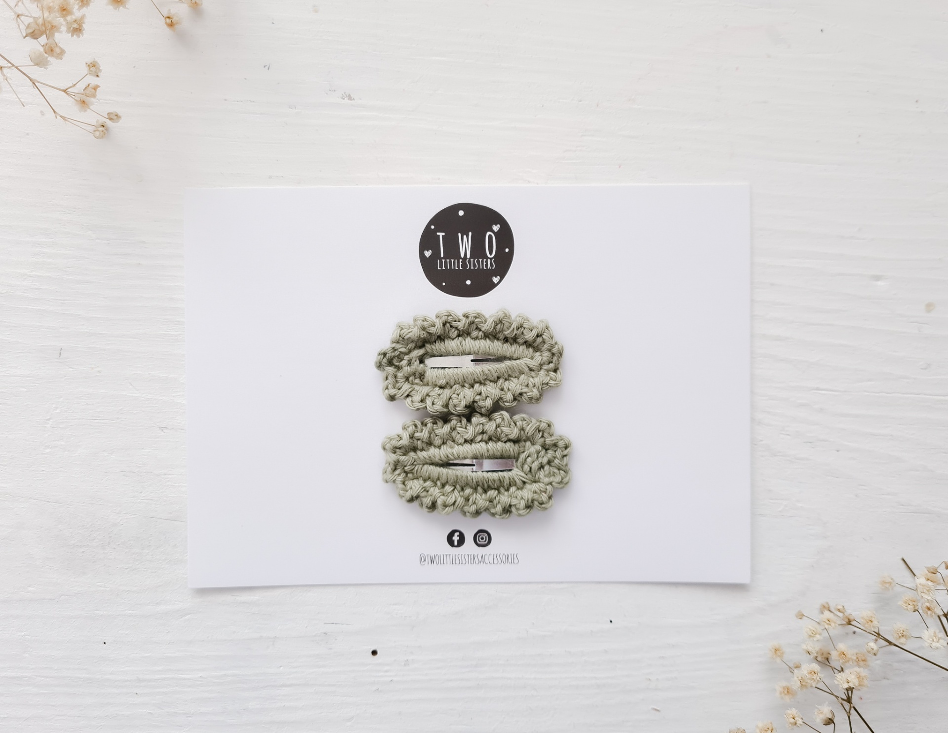 Conjunto de dois prendedores de cabelo verde-acinzentados sobre cartolina com logótipo