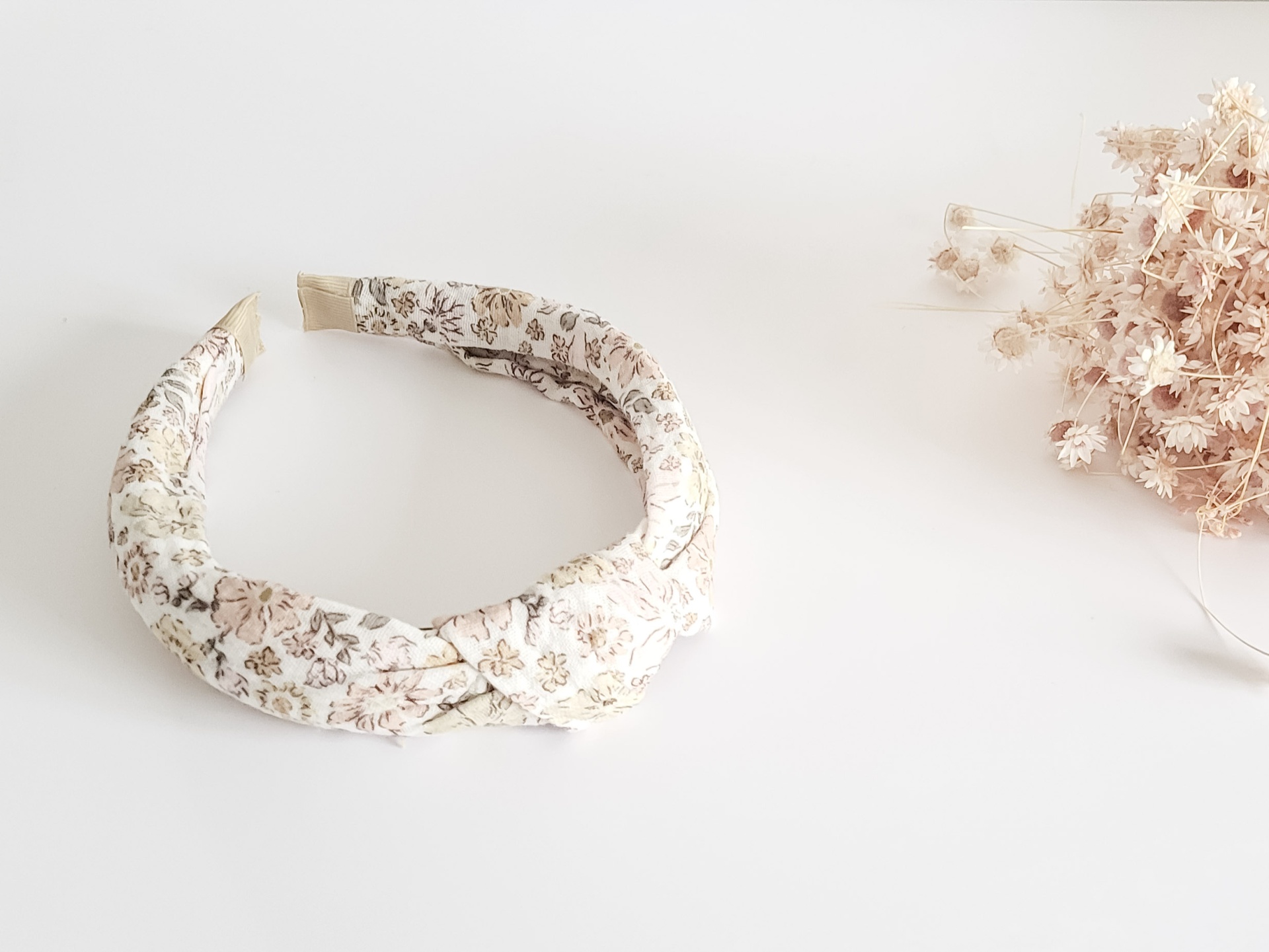 Aro de cabelo com padrão floral bege e castanho e flores secas ao lado