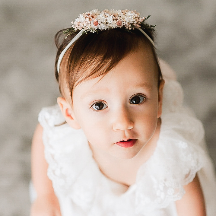 Bebé com vestido branco e faixa de cabelo com flores cor-de-rosa e brancas