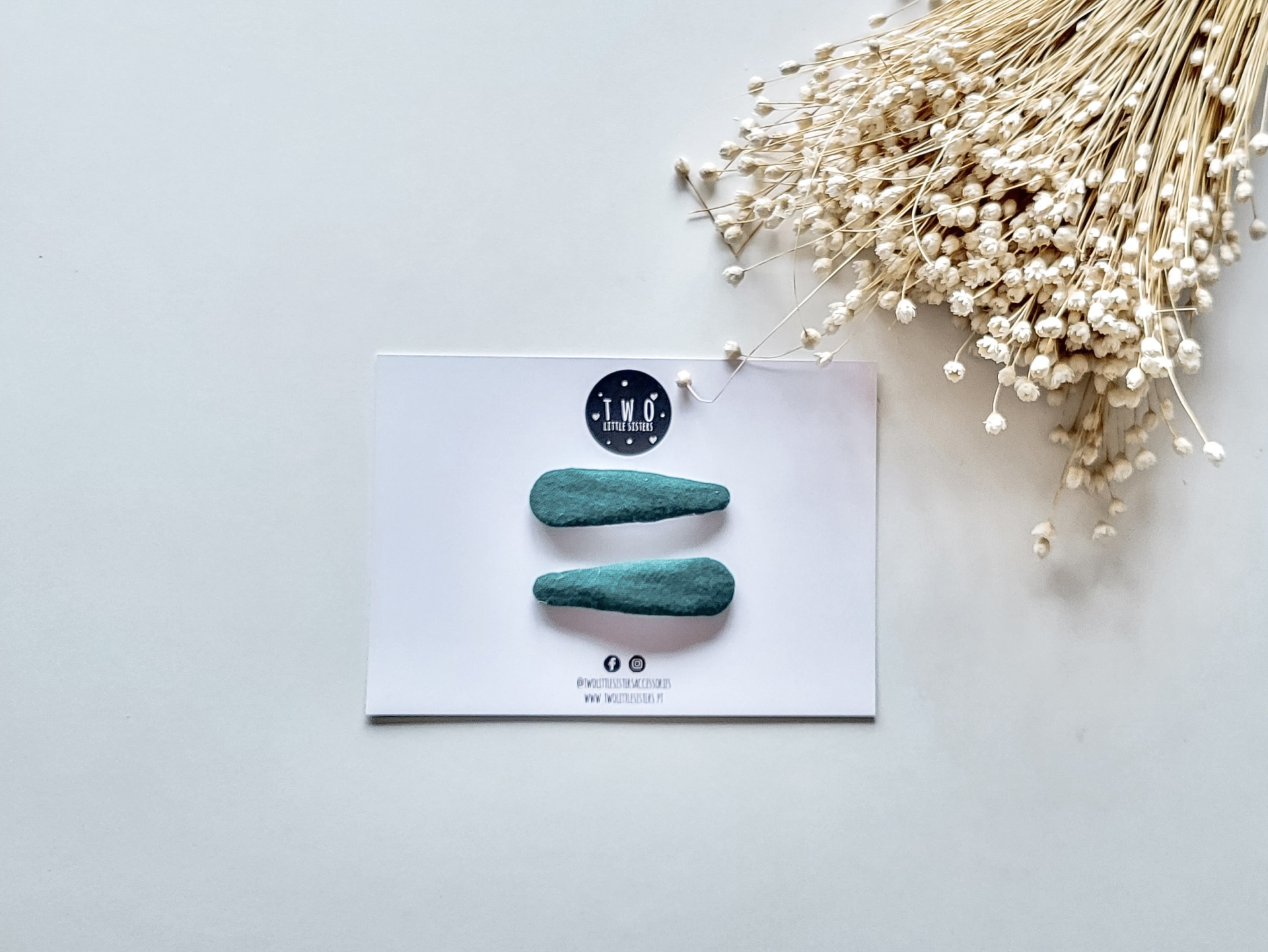 grampos de cabelo azuis esverdeados em cartão branco com flores secas brancas ao lado