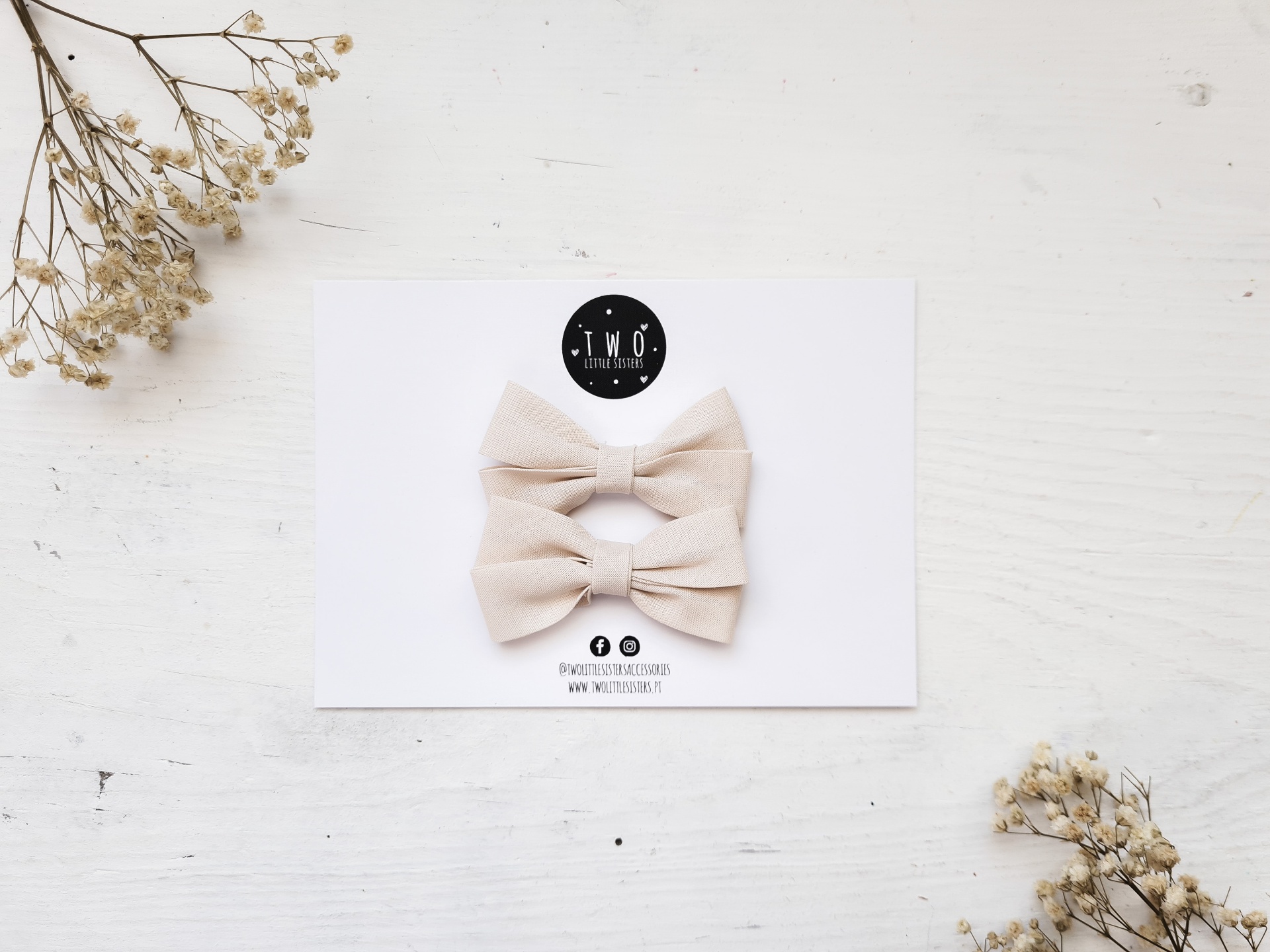 Ganchos para cabelo em forma de laço bege sobre cartolina branca com logotipo TMO Handmade, flores secas ao redor.