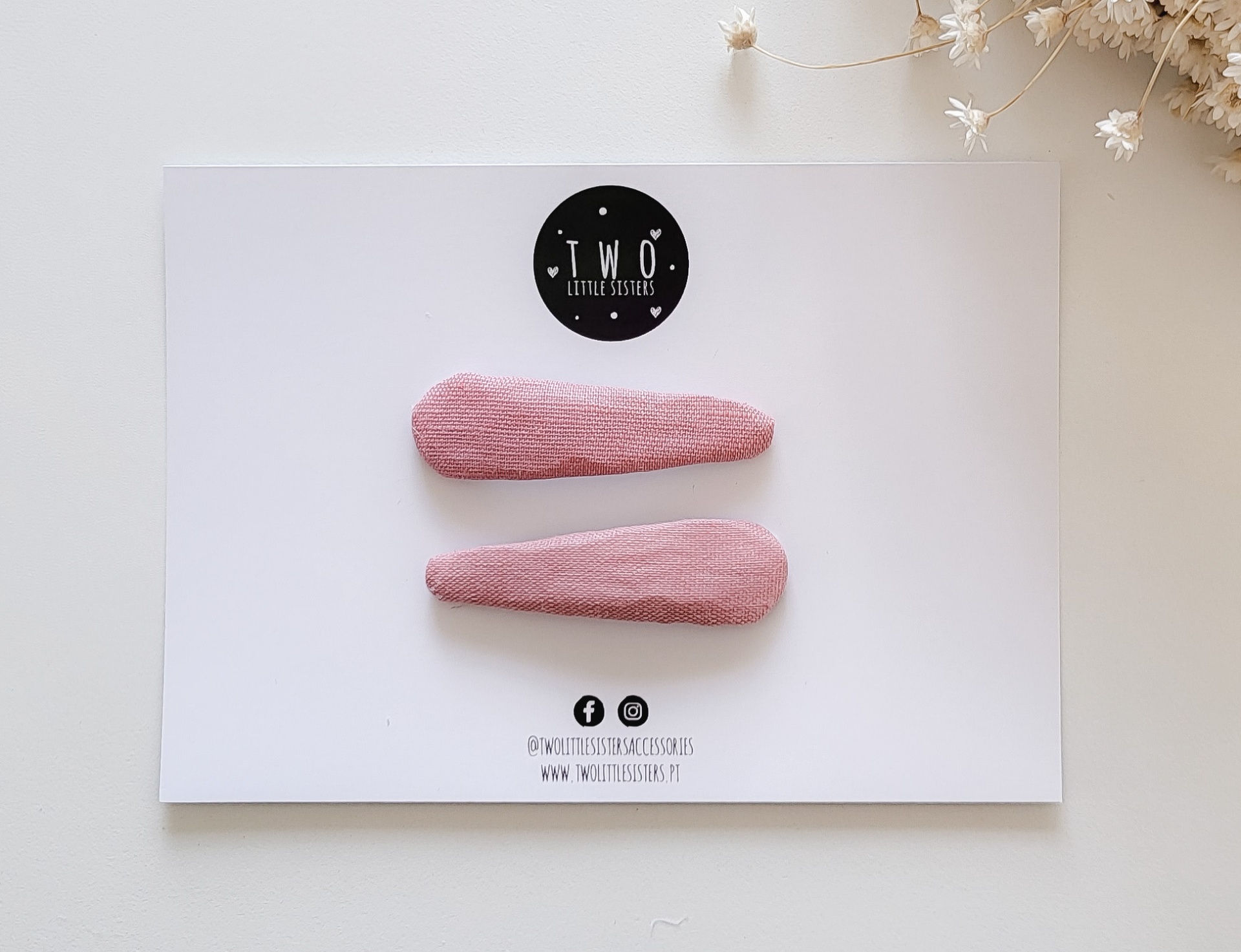 Dois ganchos de cabelo rosa em cartão branco com logotipo e texto