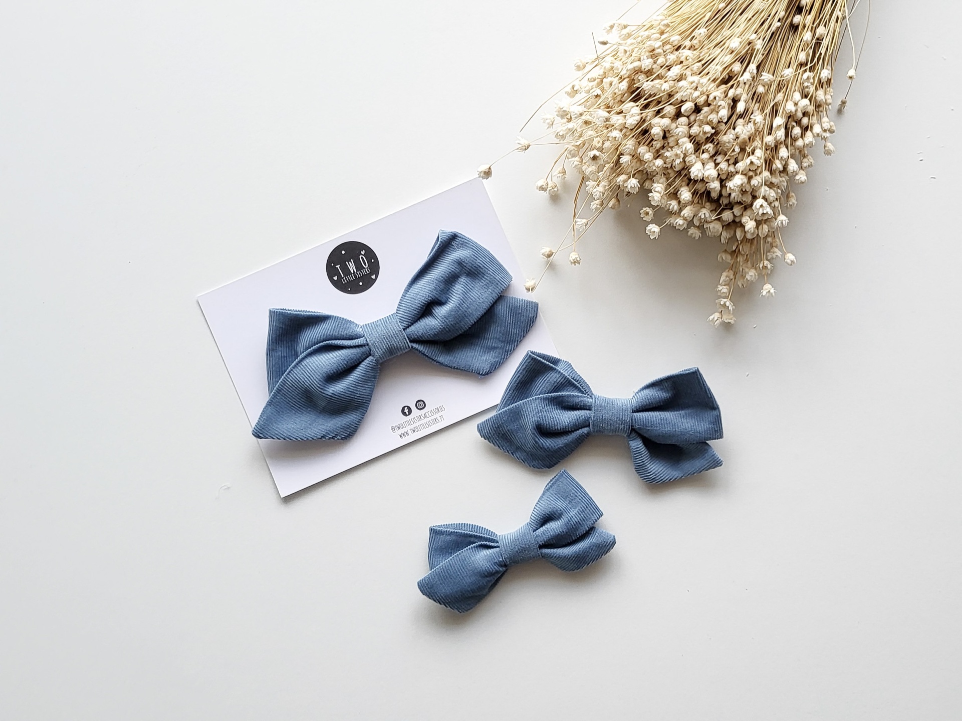 Laços de tecido azul e flores secas sobre superfície branca