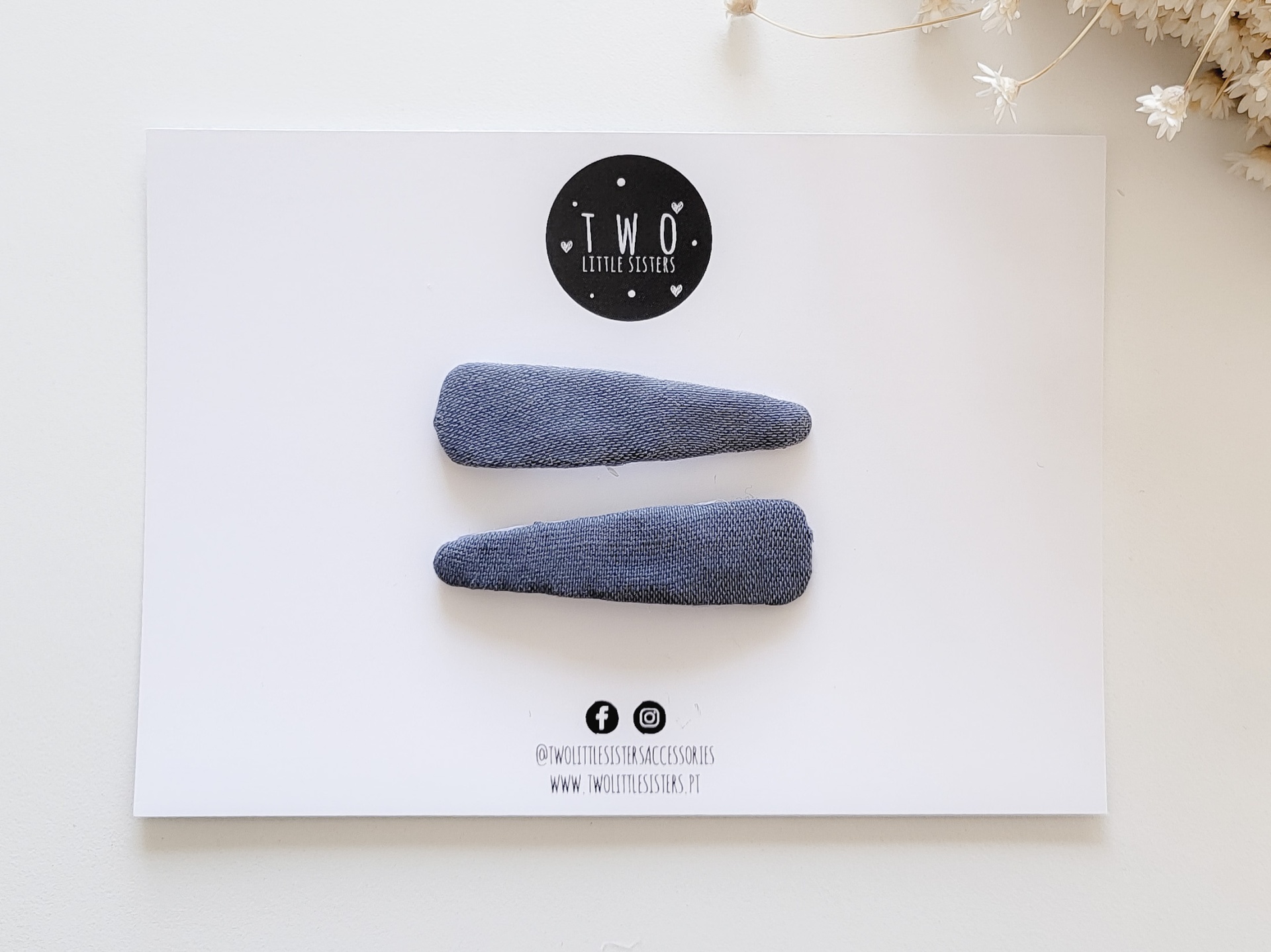 Conjunto de dois ganchos de cabelo em tecido azul num cartão branco com logótipo preto