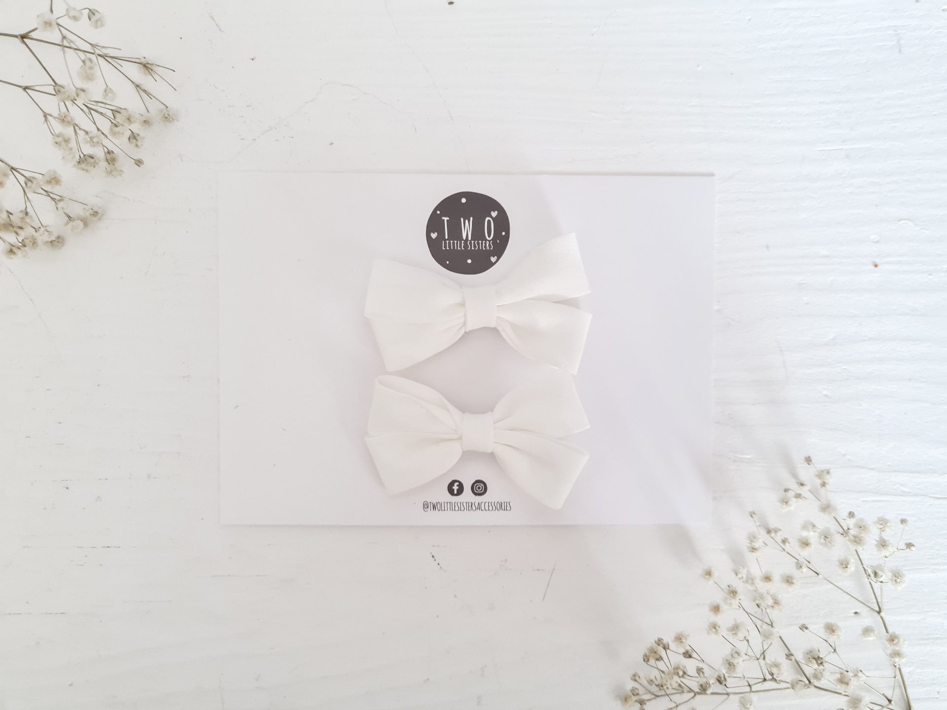 Dois laços brancos de tecido em cartão branco com logotipo, em fundo branco com flores secas