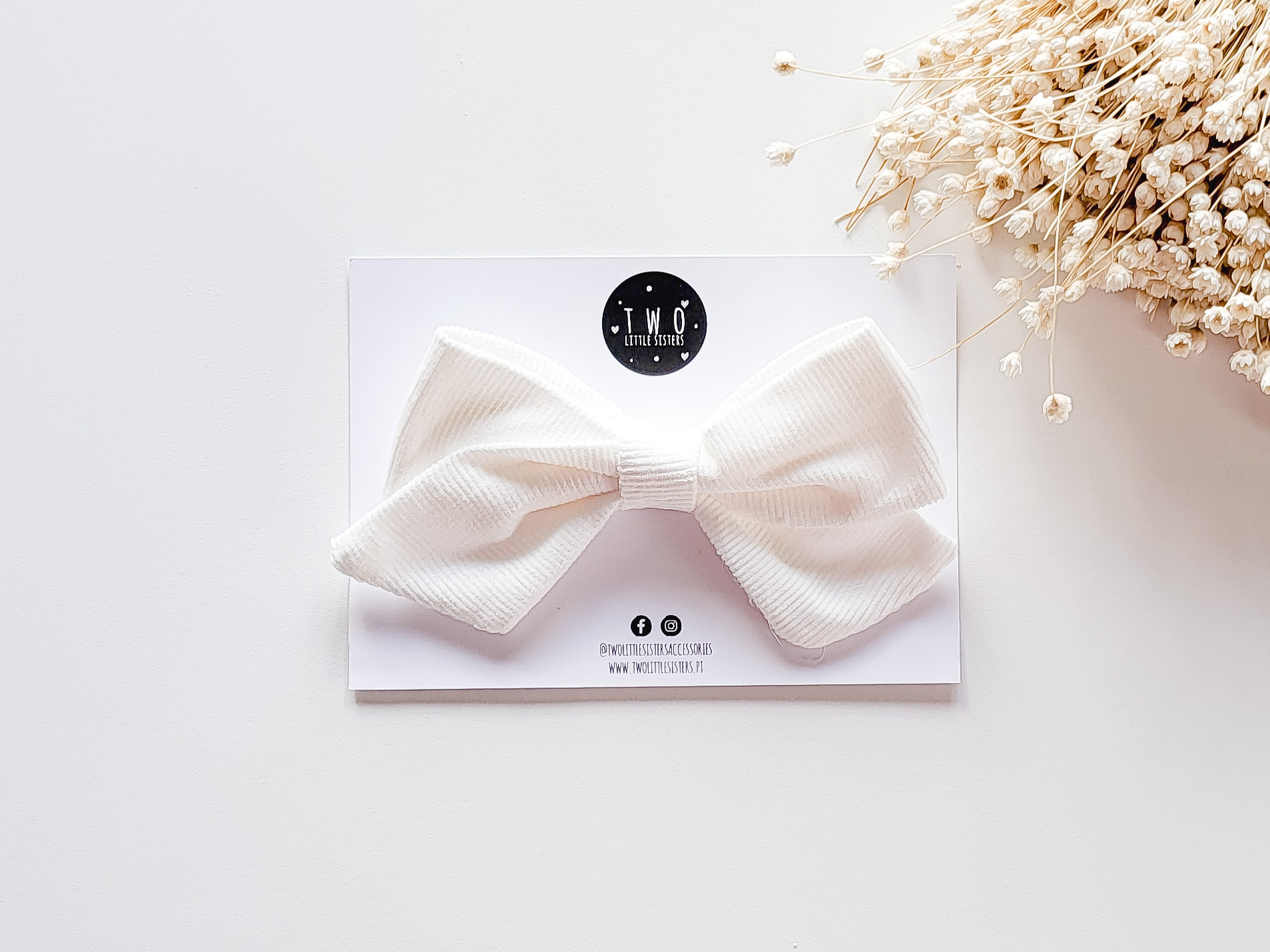 Lacinho de tecido branco em cartão branco com logotipo TMO e flores secas