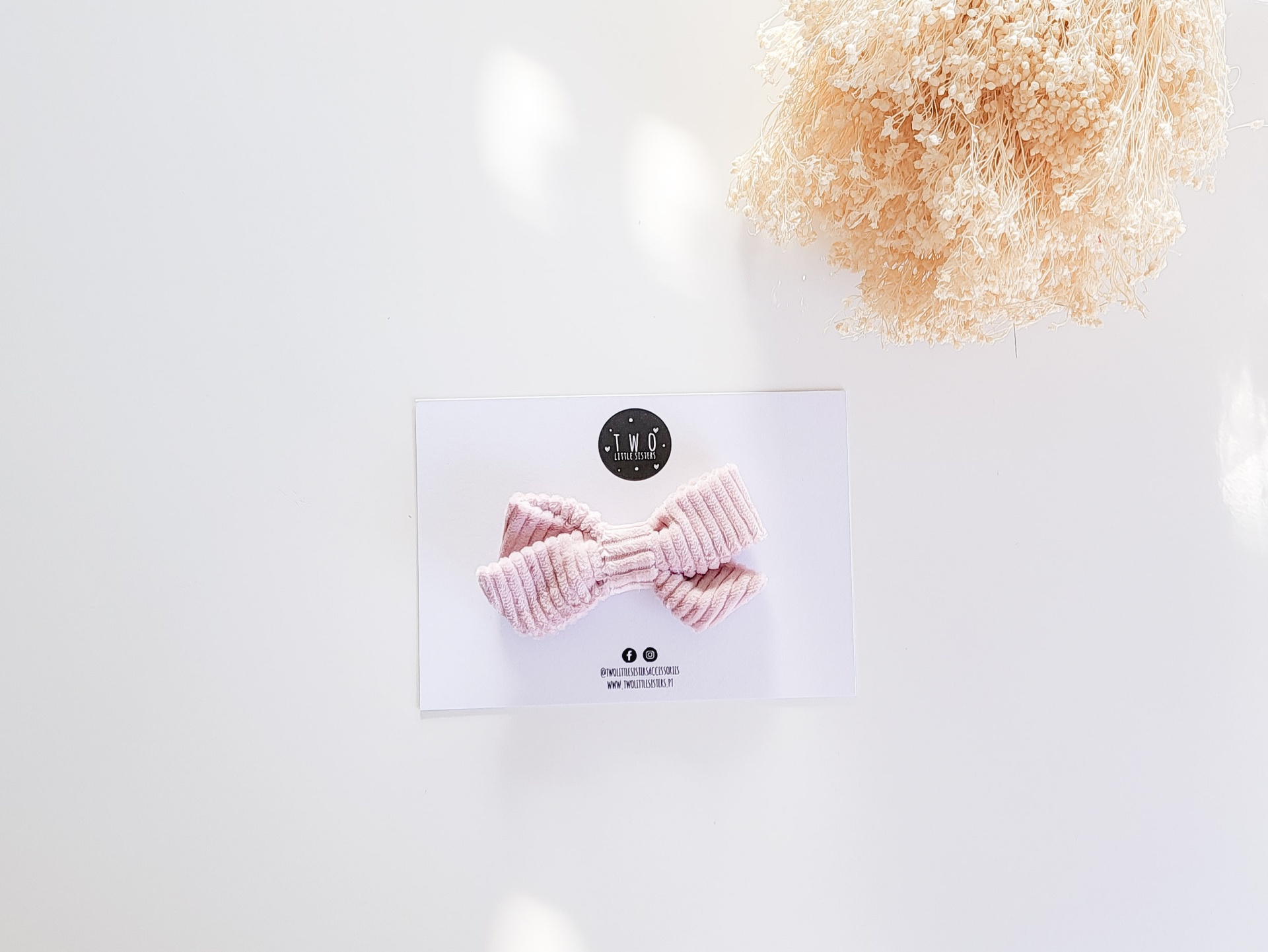 Laço de cabelo cor-de-rosa claro em tecido canelado sobre cartão branco com logótipo T.W.F