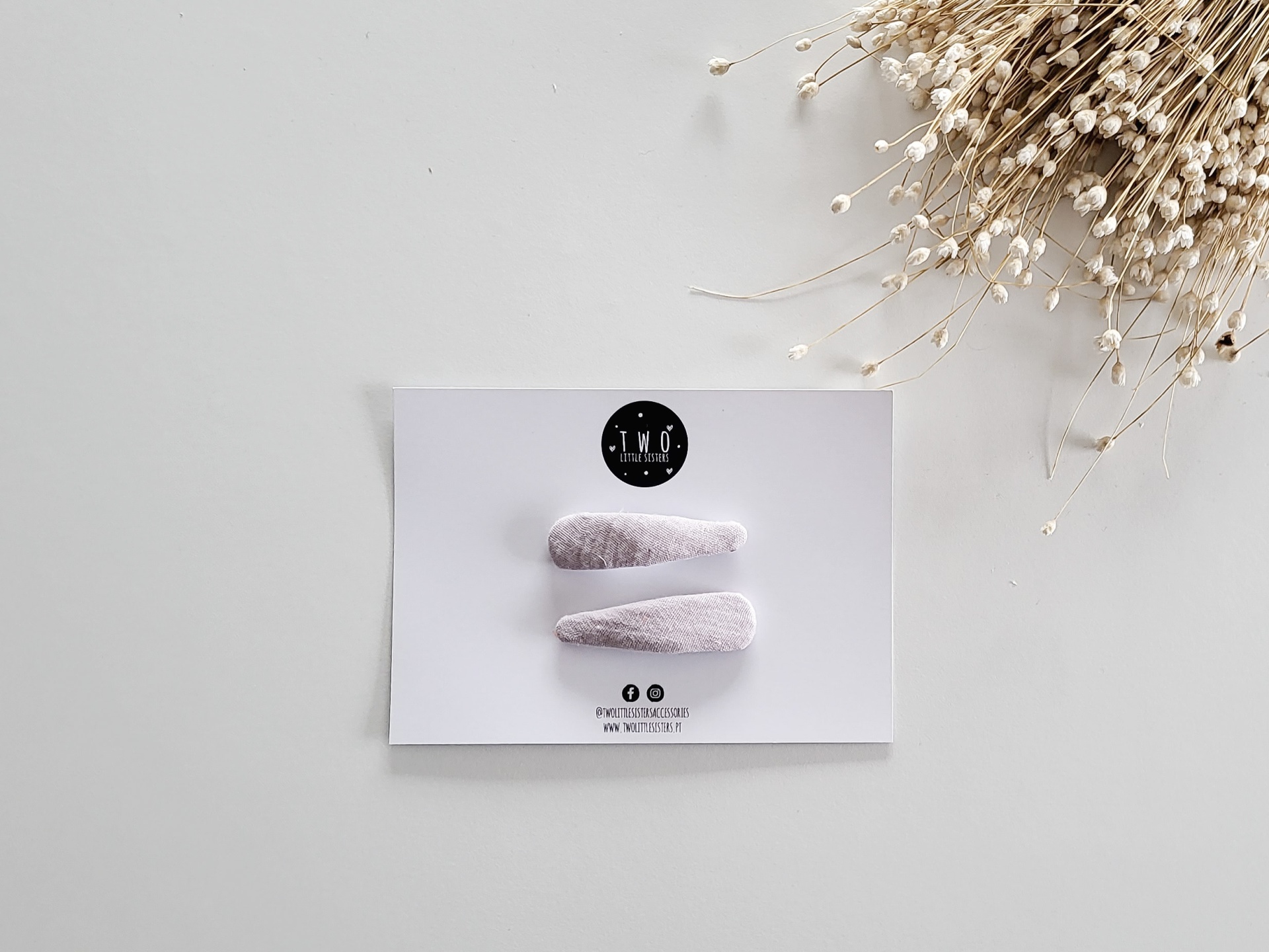 duas presilhas de cabelo cor de rosa claro em cartão branco com flores secas ao lado