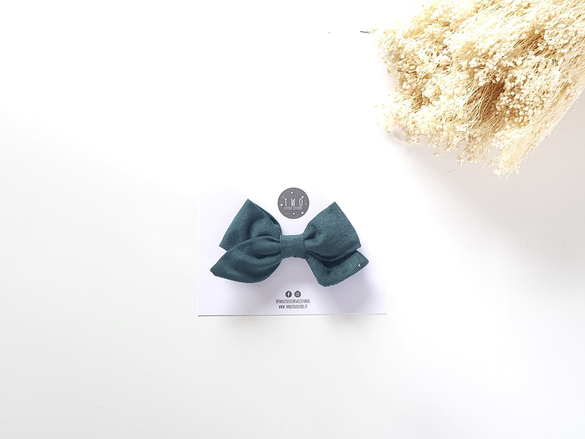 Gravata borboleta azul escuro numa cartolina branca com logótipo 1+1 e ramos secos ao lado.