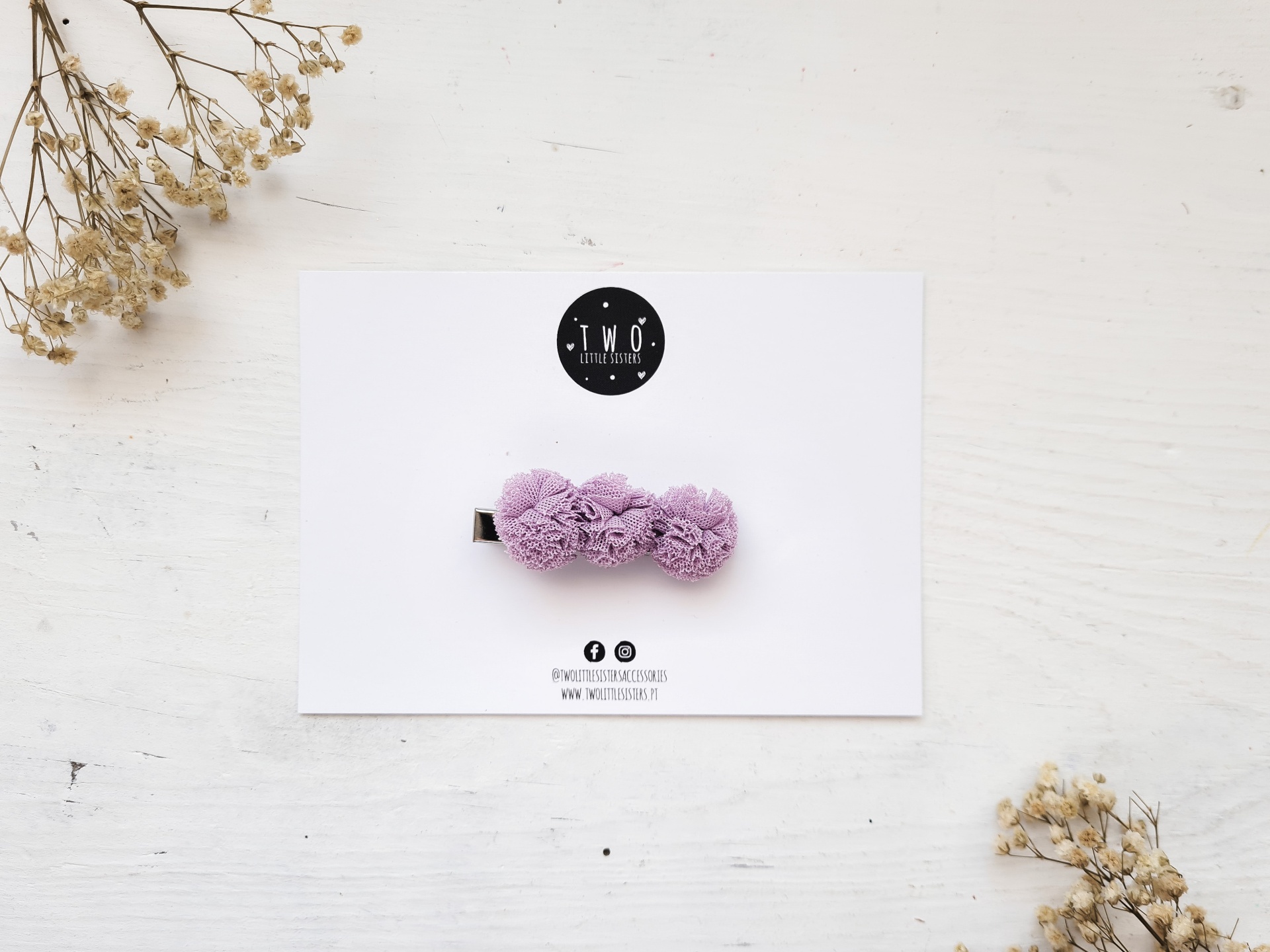 Prendedor de cabelo com flores lilás em cartão branco sobre superfície branca