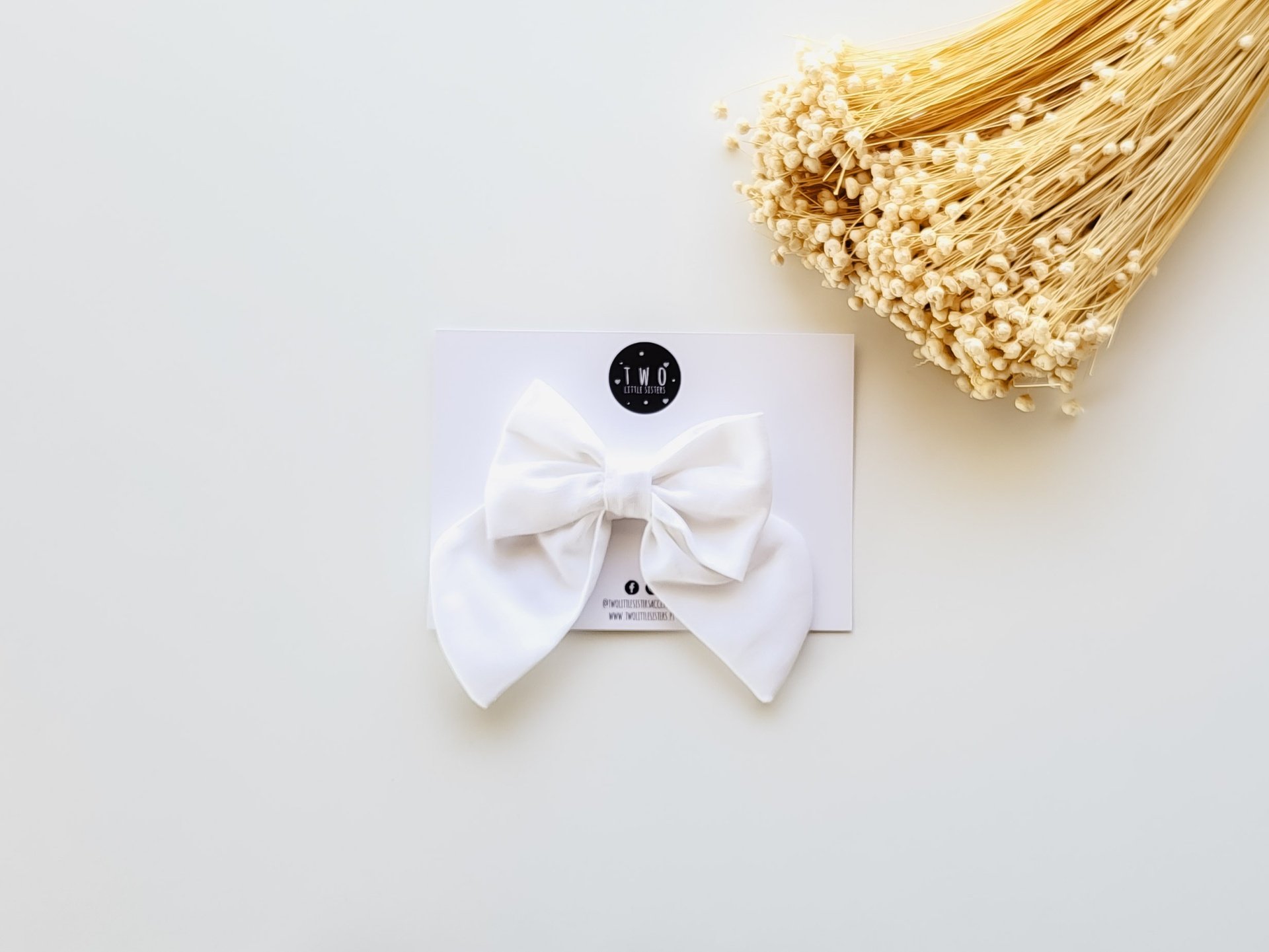 Laço branco de tecido sobre cartão branco com flores secas ao lado