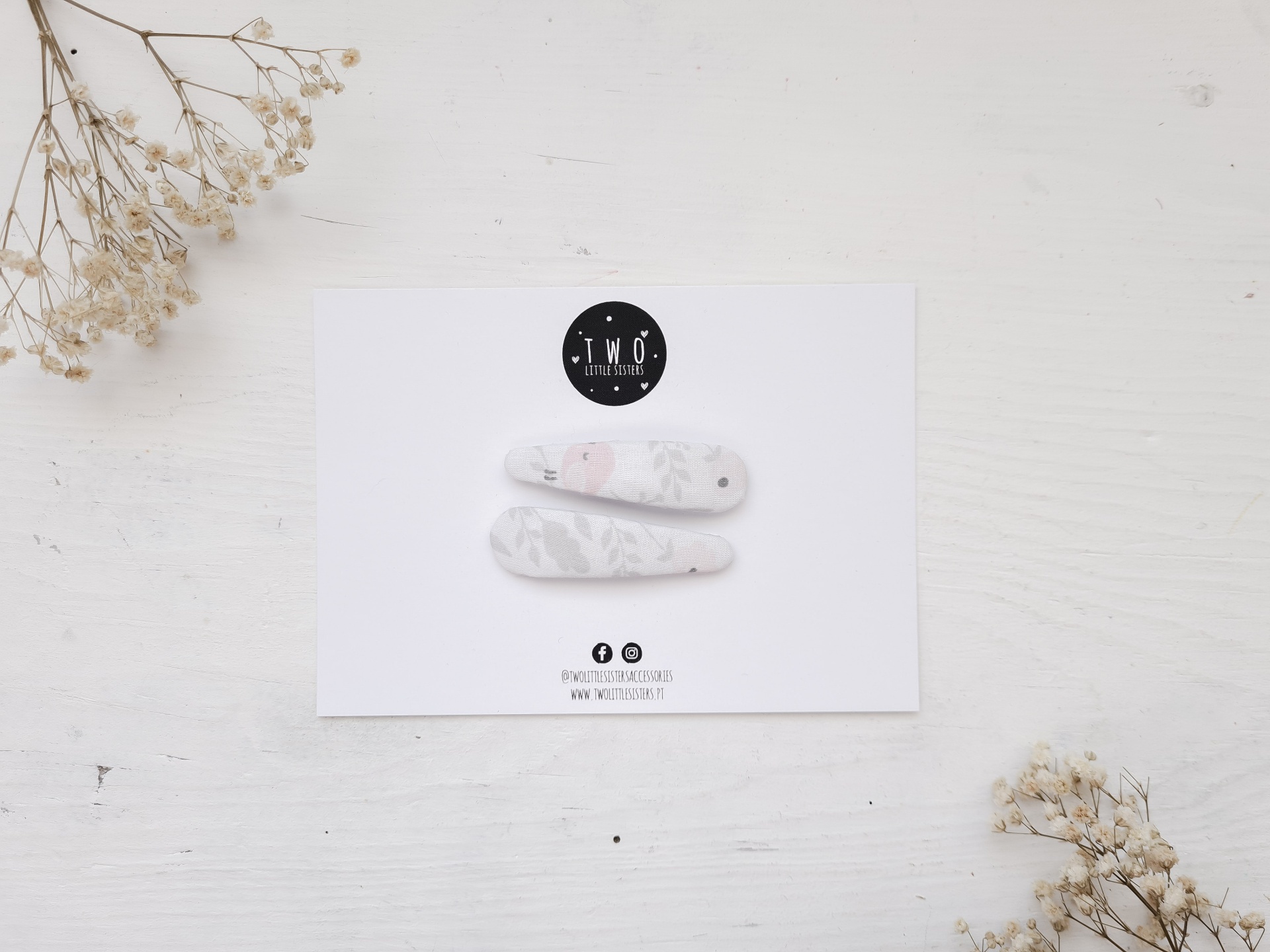 Par de molas de cabelo brancas com padrão cinza num cartão branco com logo TMQ