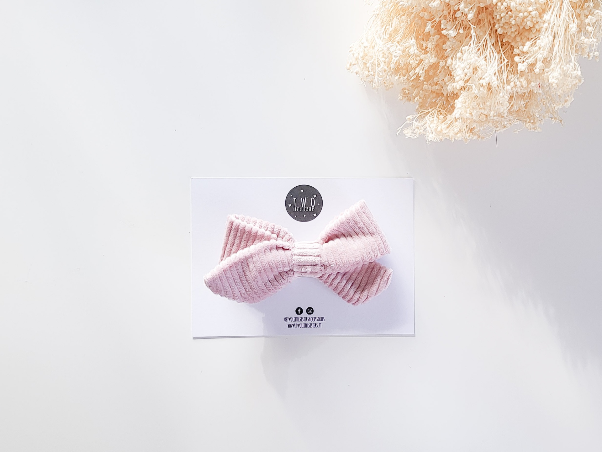 Prendedor de cabelo em laço rosa em cartolina branca com planta seca ao lado