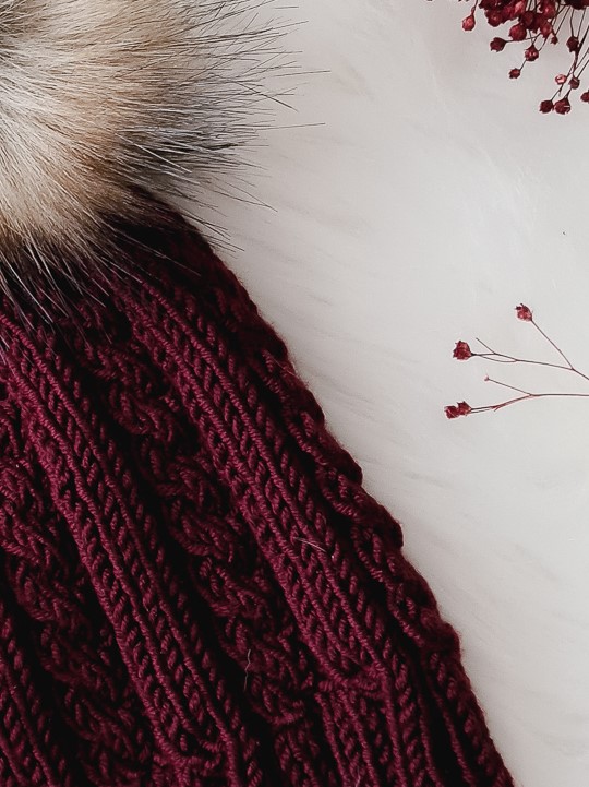 Gorro bordô de malha com pompom de pelo e flores secas ao lado