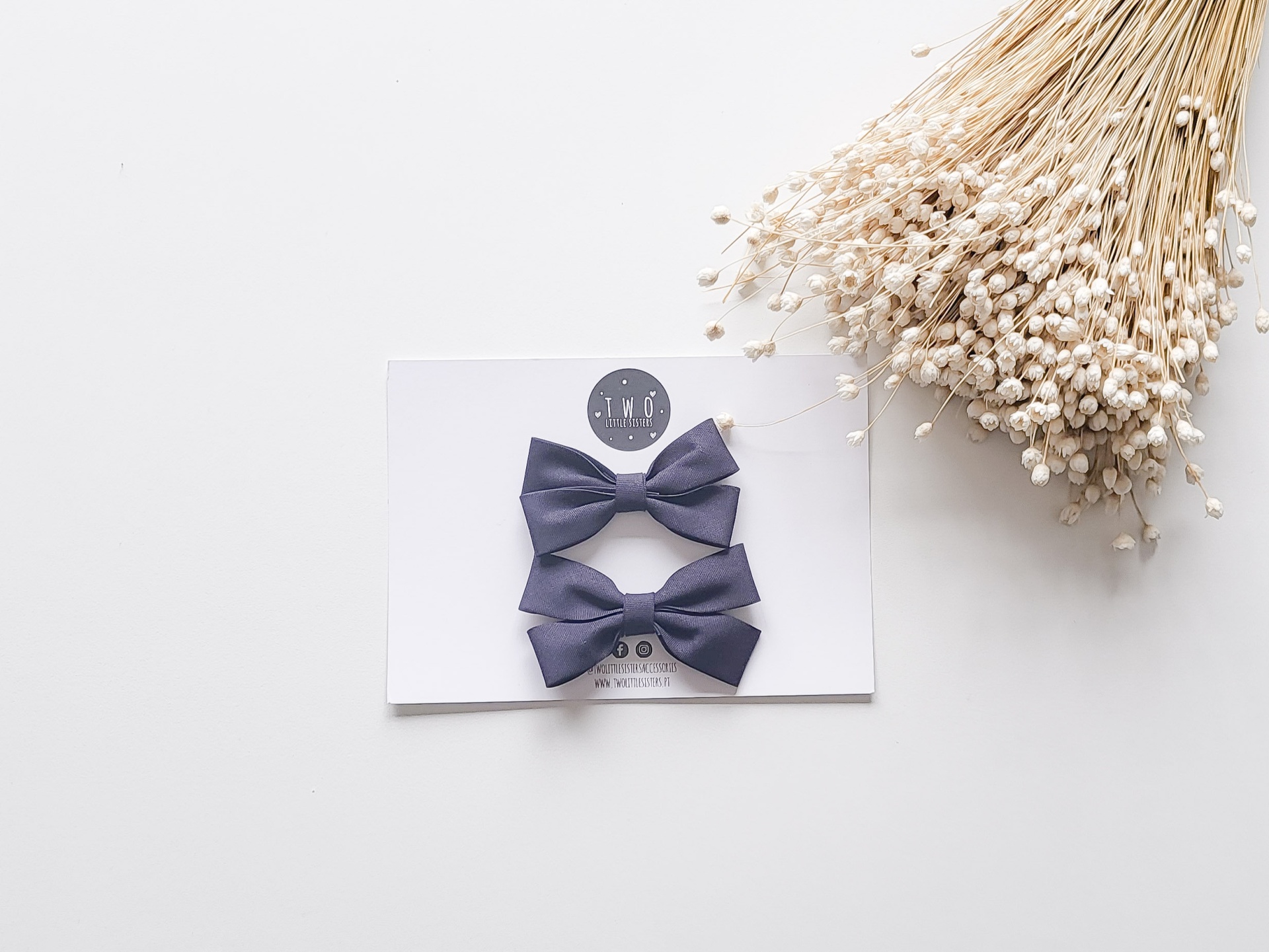 Dois laços azuis-acinzentados numa cartolina com flores secas ao lado