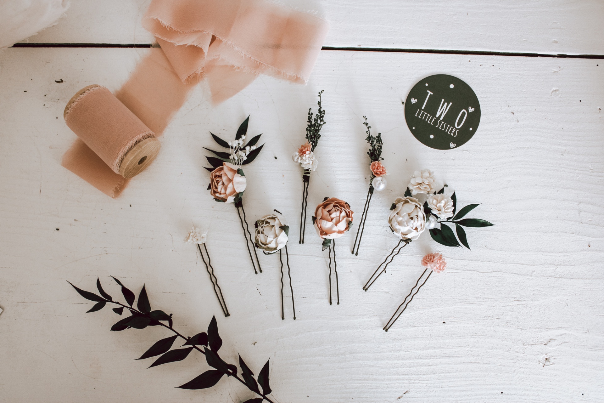 Grampos de cabelo decorativos com flores e folhas sobre mesa branca