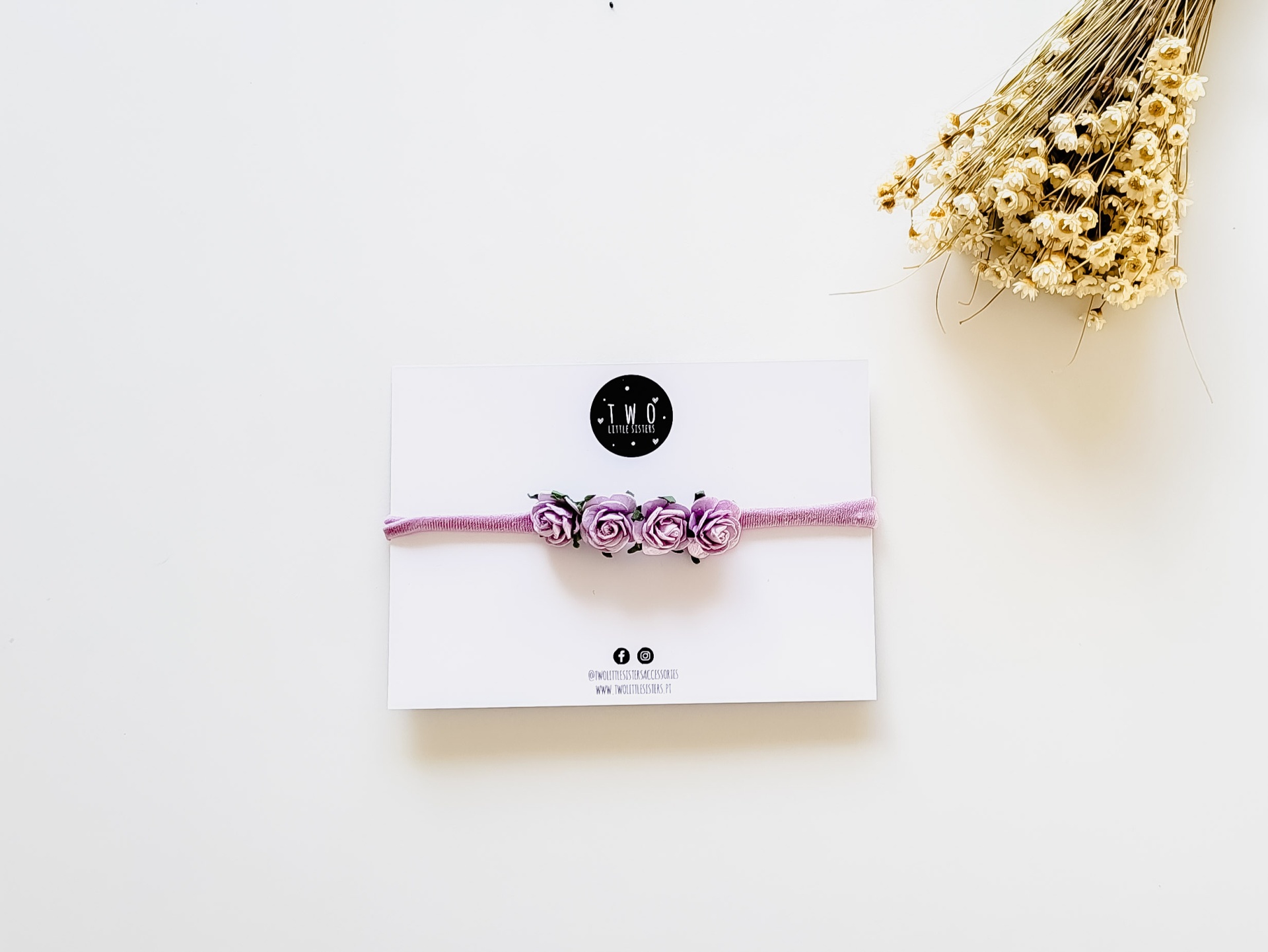 Pulseira cor-de-rosa com flores de tecido roxo e rosa apresentada em cartão branco com flores secas ao lado