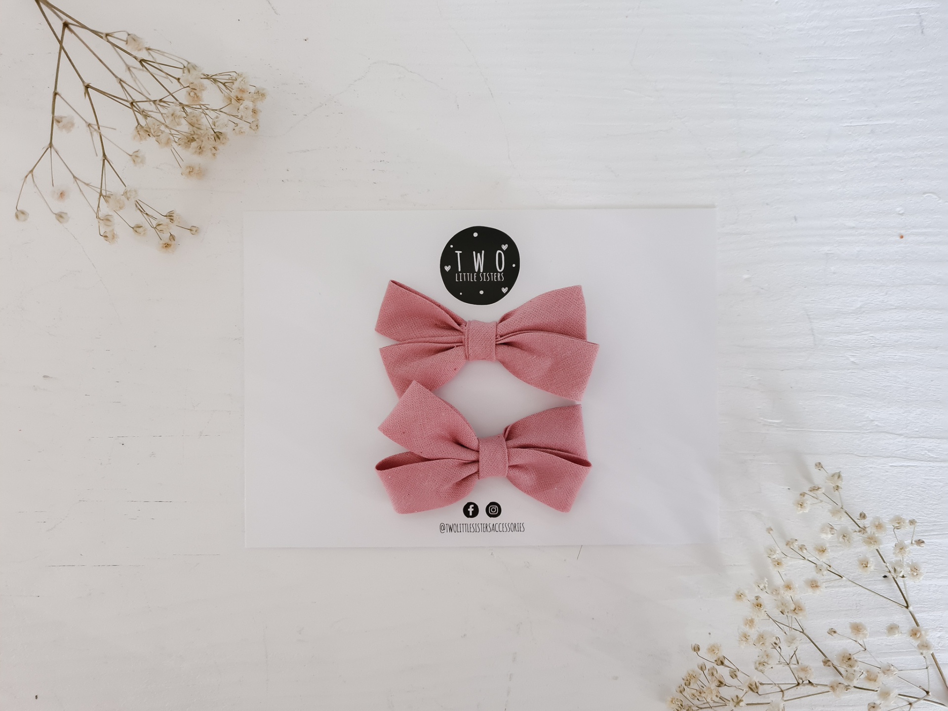 Dois laços cor de rosa em tecido sobre cartão branco com logo e ícones sociais