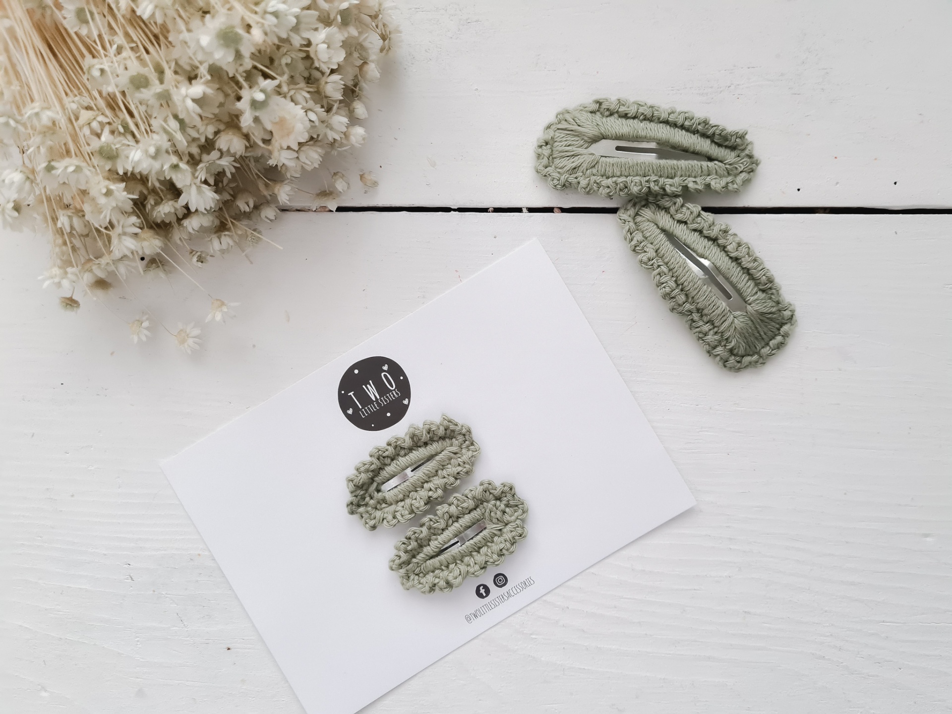 Presilhas de cabelo verdes felpudas sobre cartão e superfície branca com ramo de flores secas