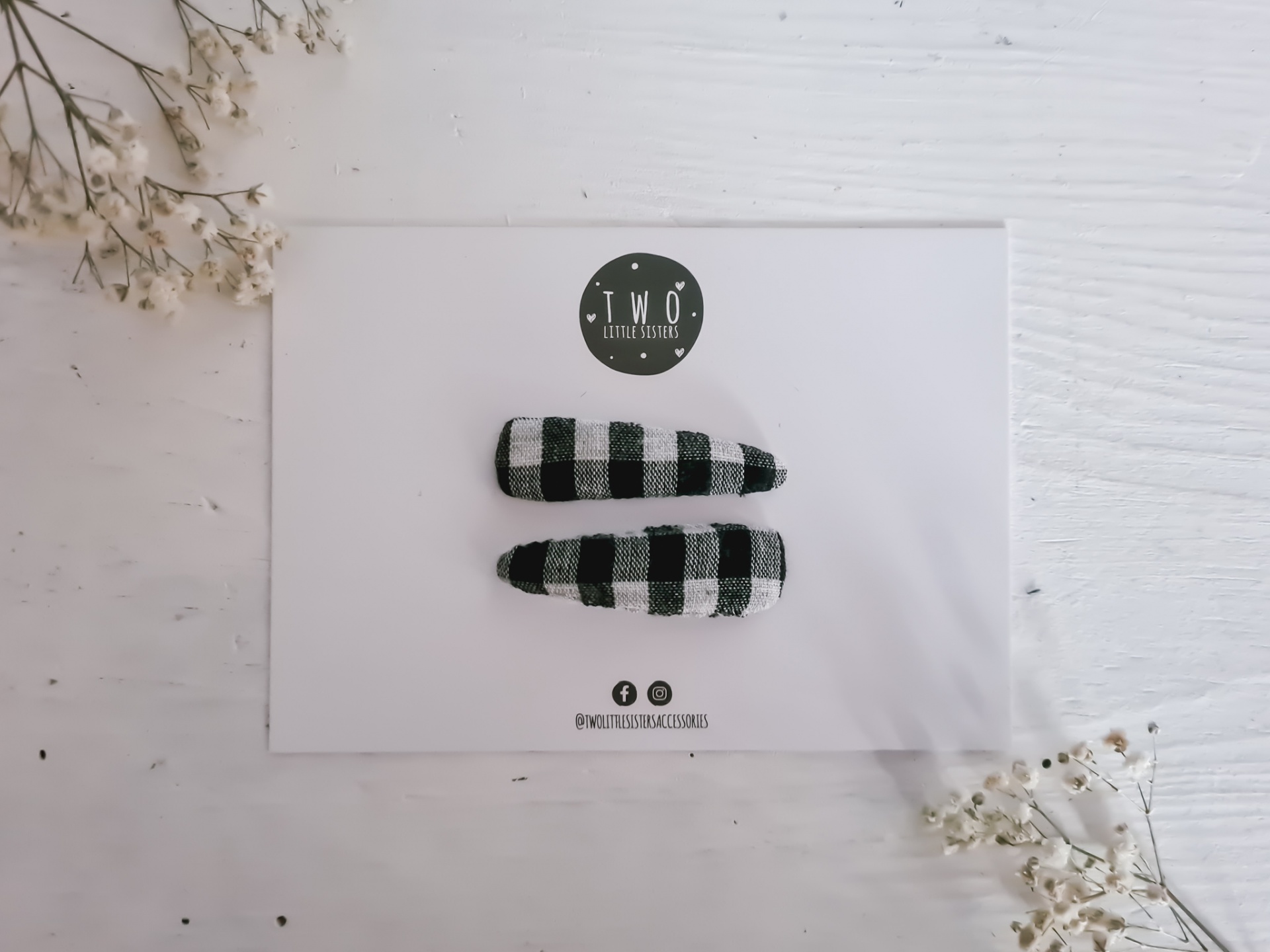 Dois ganchos de cabelo xadrez preto e branco em cartão branco com logótipo circular T.W.O