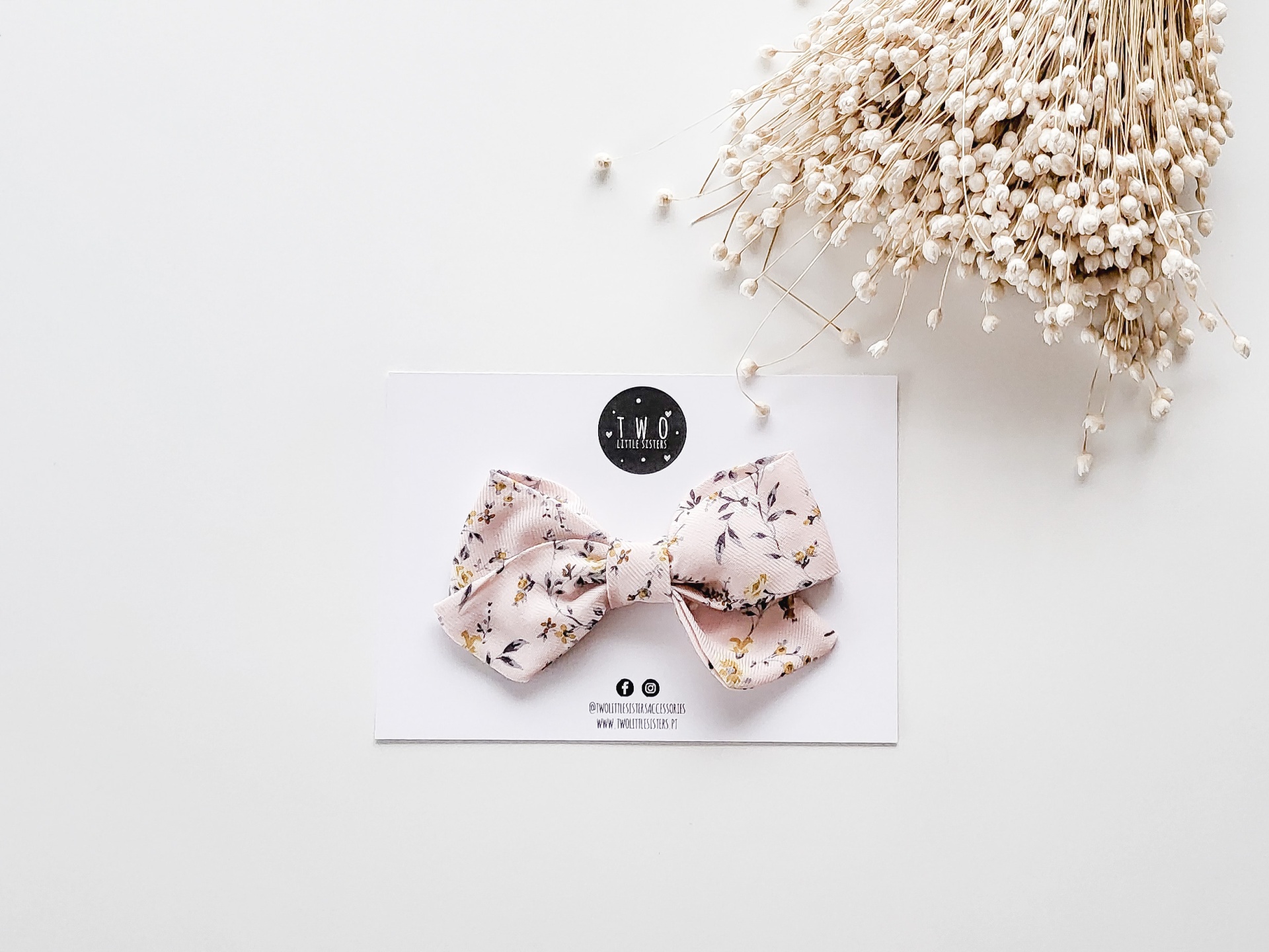 Laço floral cor de rosa claro com cartão e ramos de flores secas ao lado