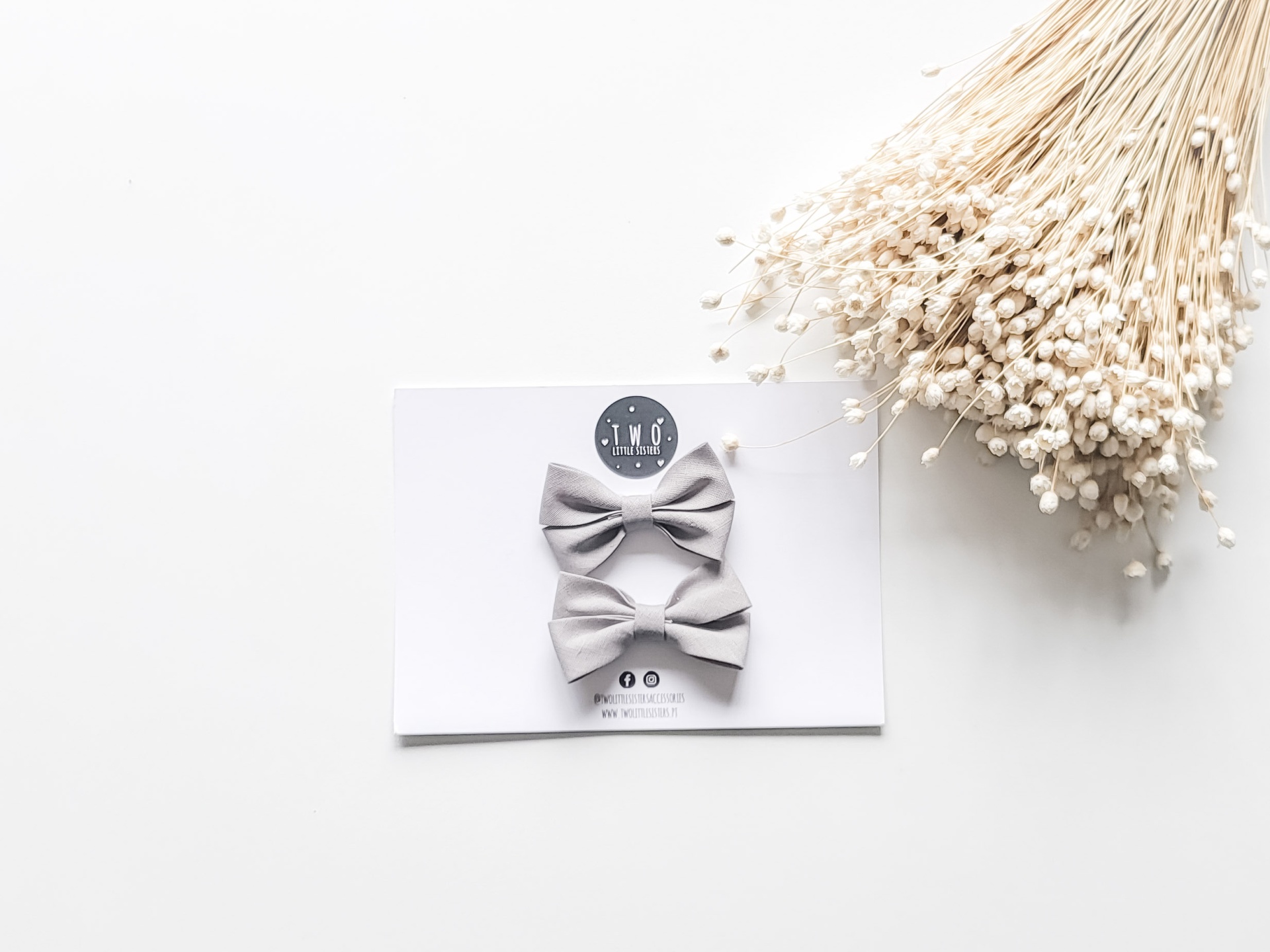 Dois laços de cabelo cinza em cartão branco com flores secas ao lado