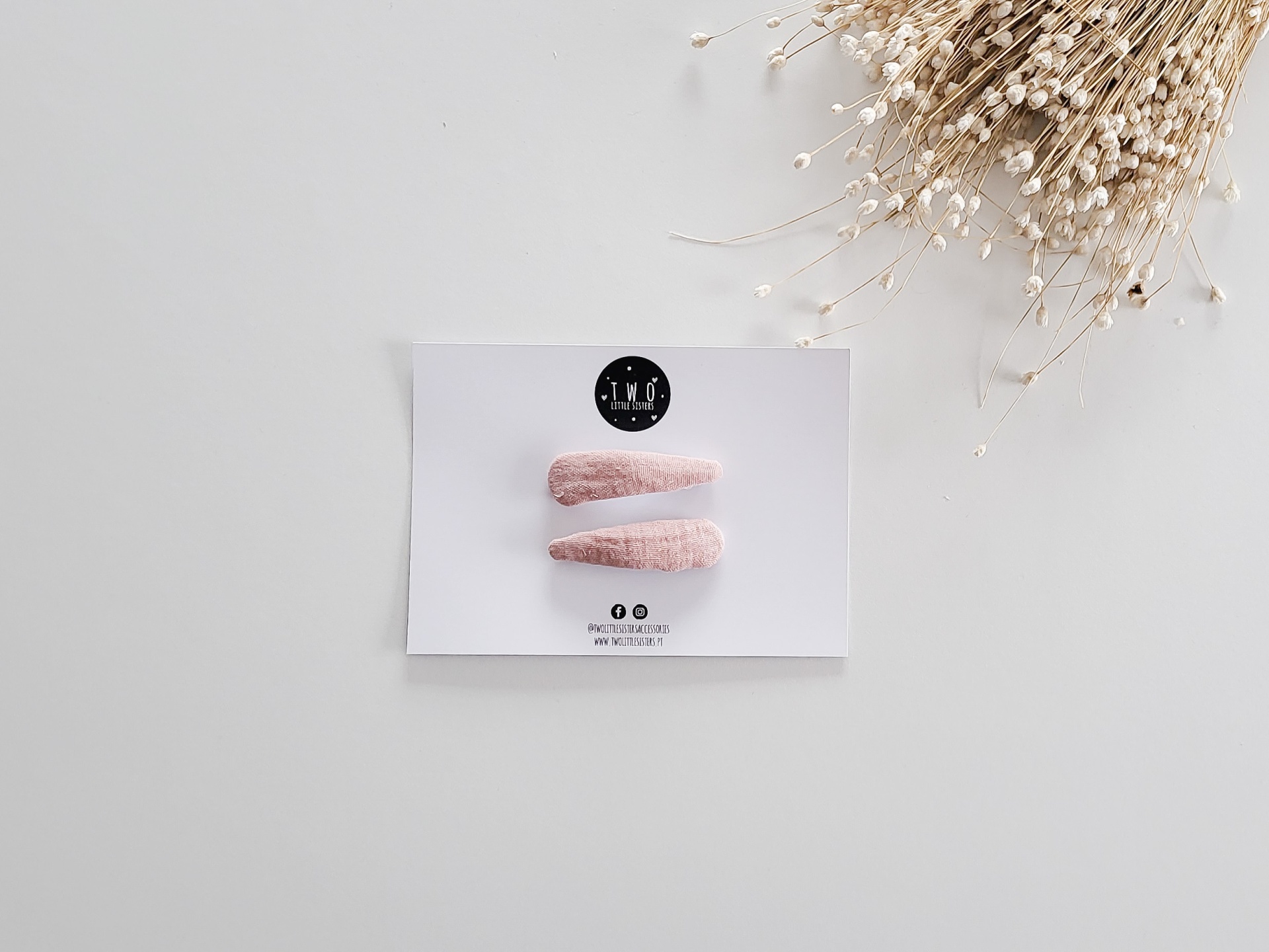 Duas presilhas de cabelo em veludo rosa num cartão branco com logo e flores secas ao lado