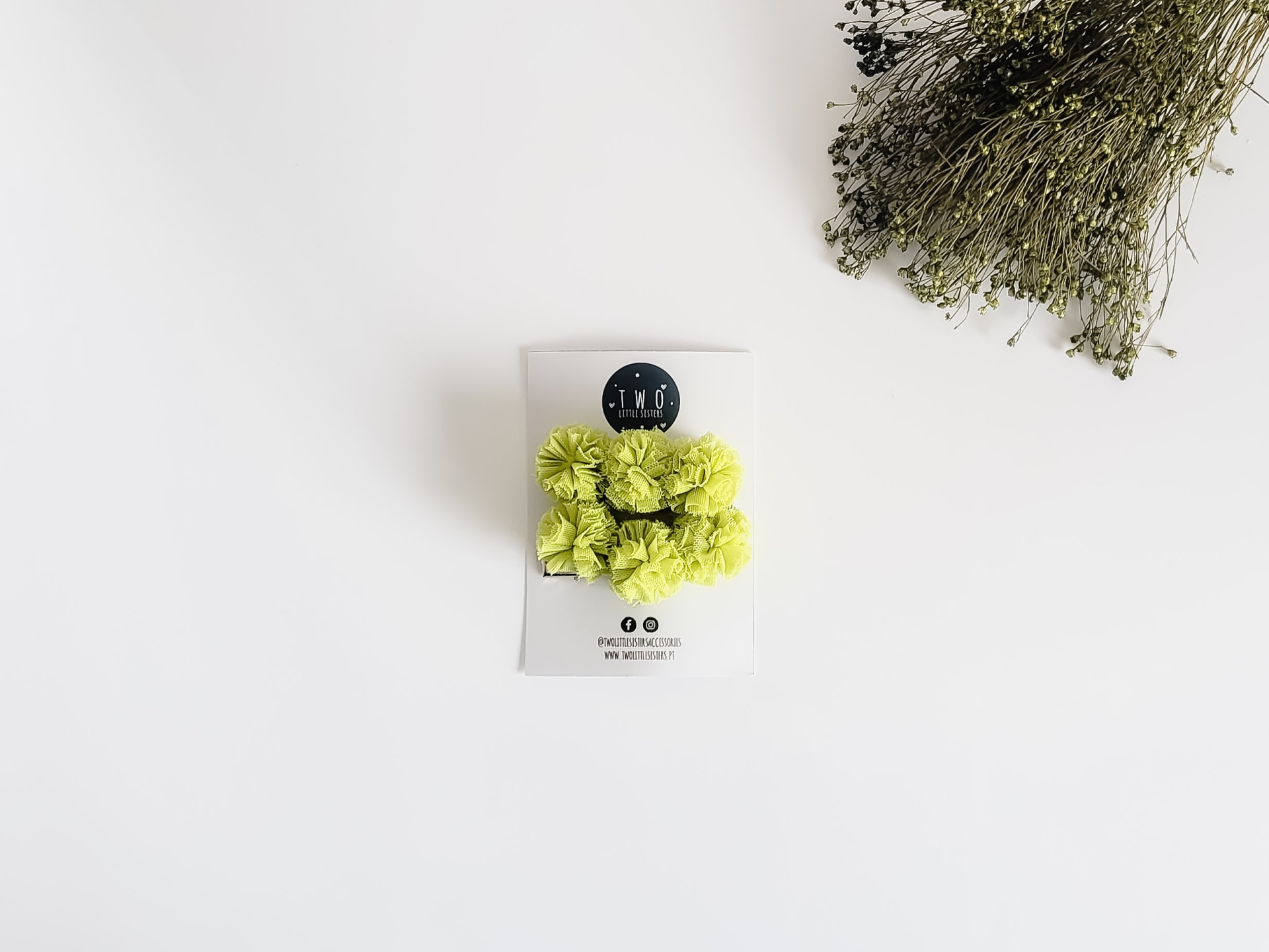 Laço de cabelo verde limão em cartolina branca com flores secas ao lado