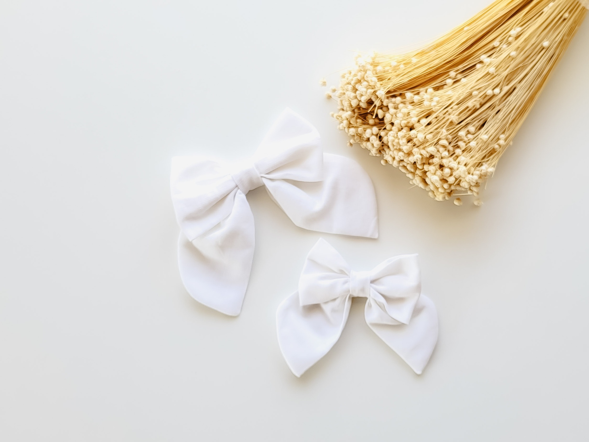 Dois laços brancos de tecido e ramo de flores secas claras sobre fundo branco