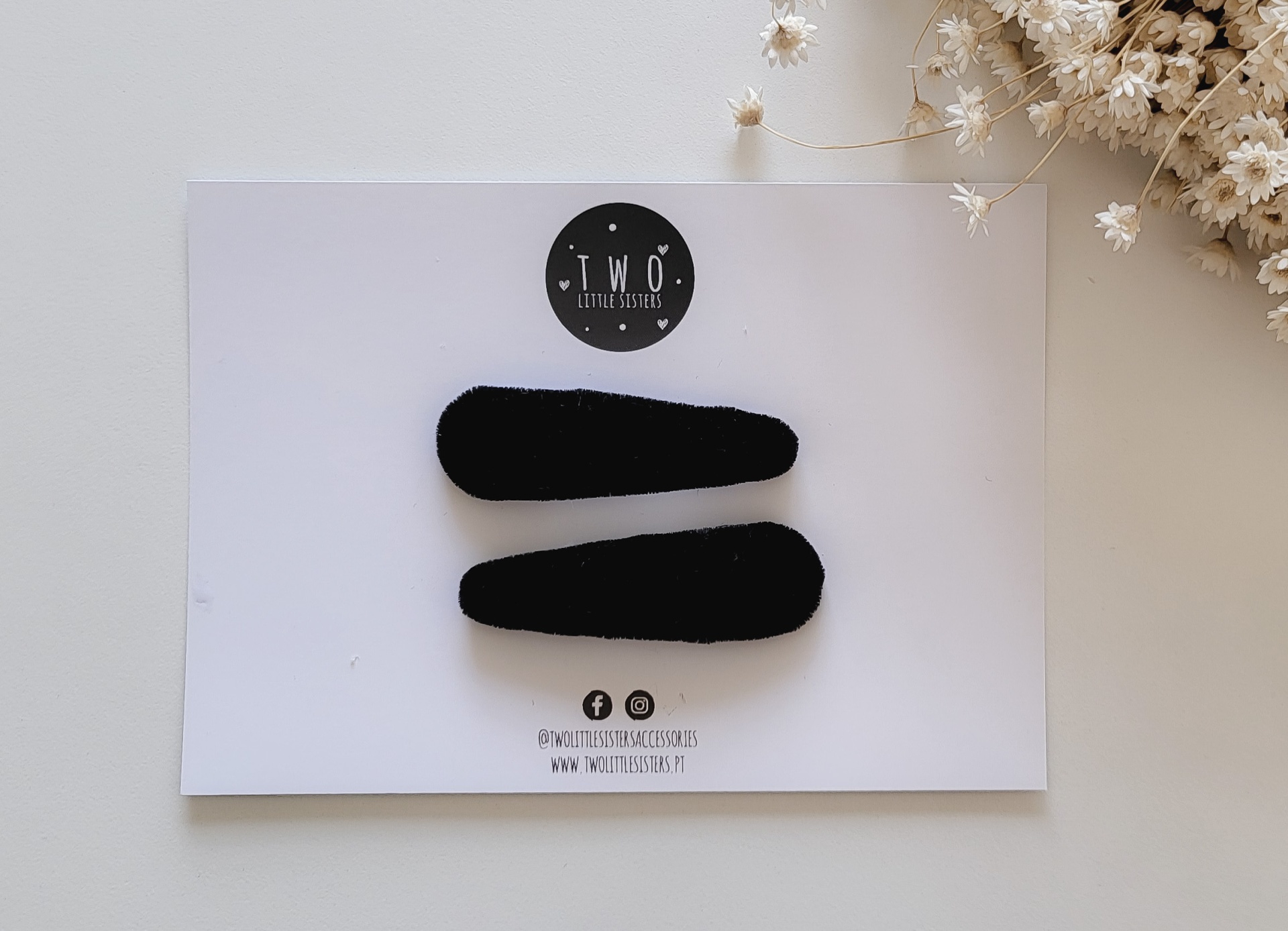 Duas presilhas pretas de veludo em cartão branco com etiqueta e flores secas ao lado