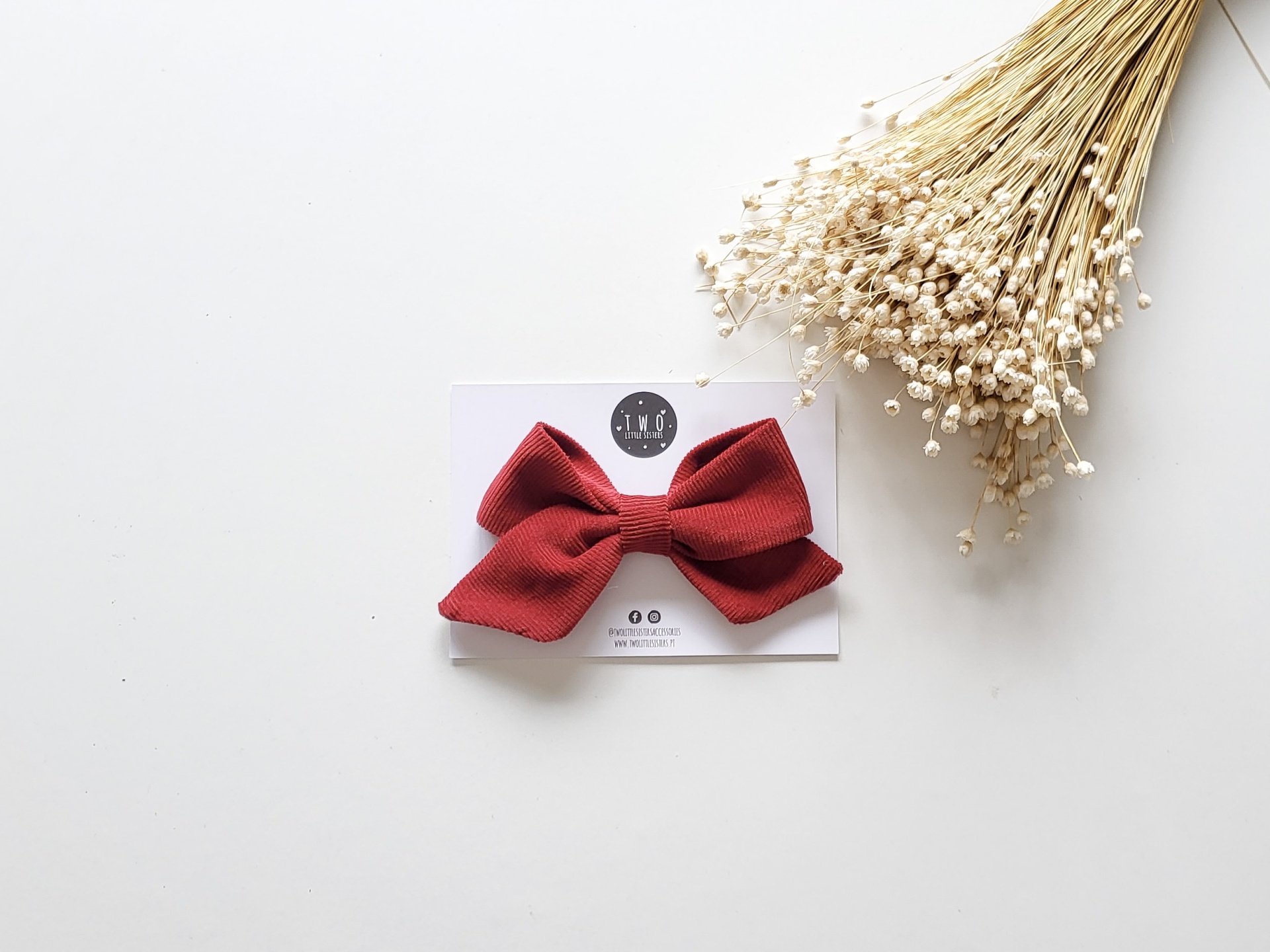 Laço vermelho em tecido canelado com cartão branco e flores secas ao lado