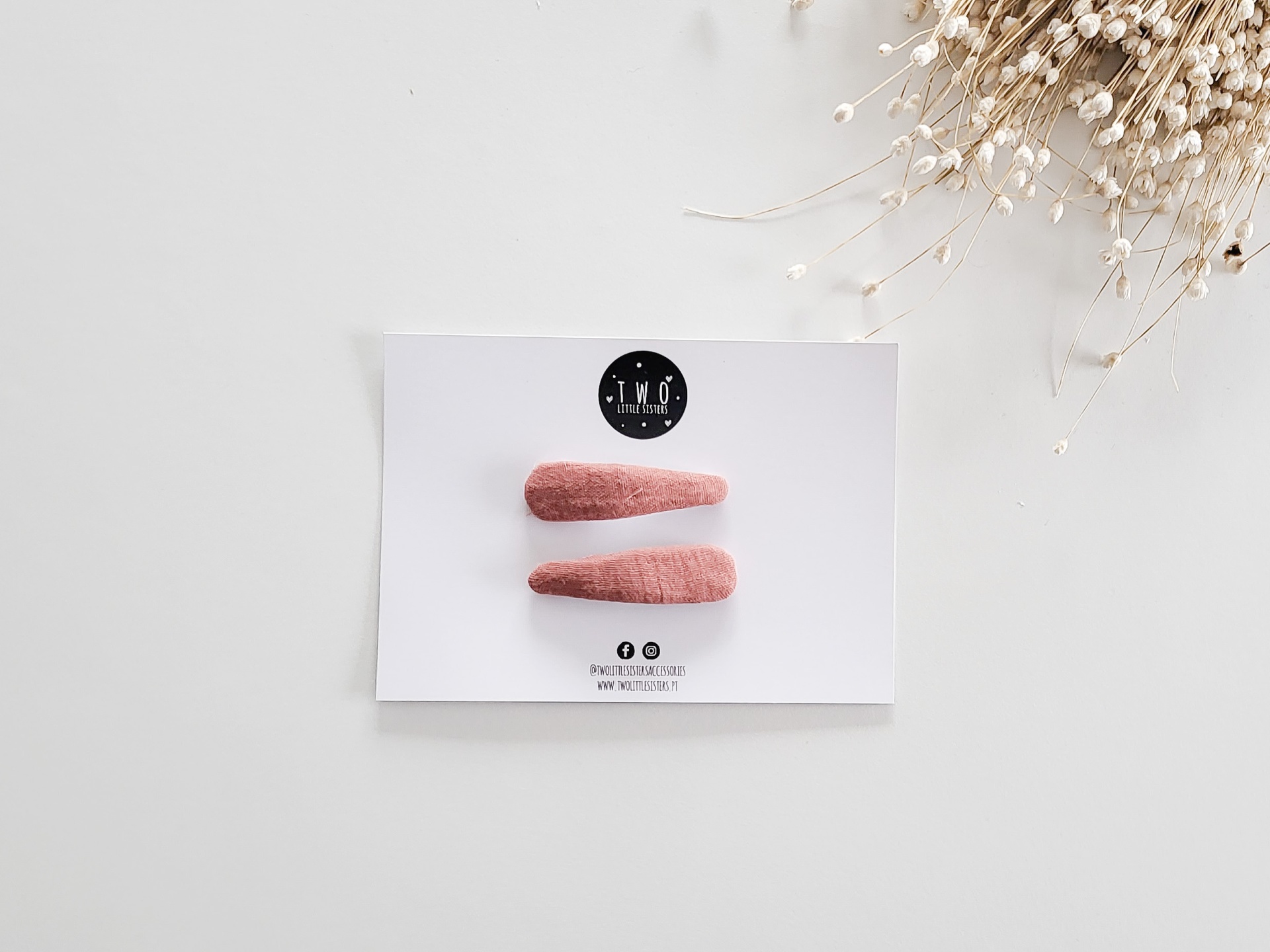 Dois ganchos de cabelo cor de rosa em tecido sobre cartão branco com texto T.M.O. THE MUSE ON