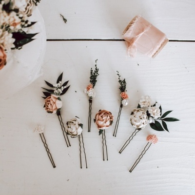 Ganchos para cabelo com flores artificiais em branco, creme e rosa sobre mesa branca de madeira