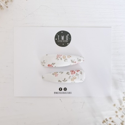 Molhas de cabelo branca com padrão floral em cartão branco com logotipo TWO LITTLE EXPLORERS e raminhos de flores secas