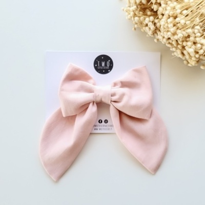 Laço cor-de-rosa em tecido preso a cartão branco com texto e flores secas ao lado.