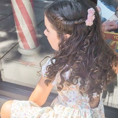Menina com cabelo cacheado e vestido floral sentada junto a janela